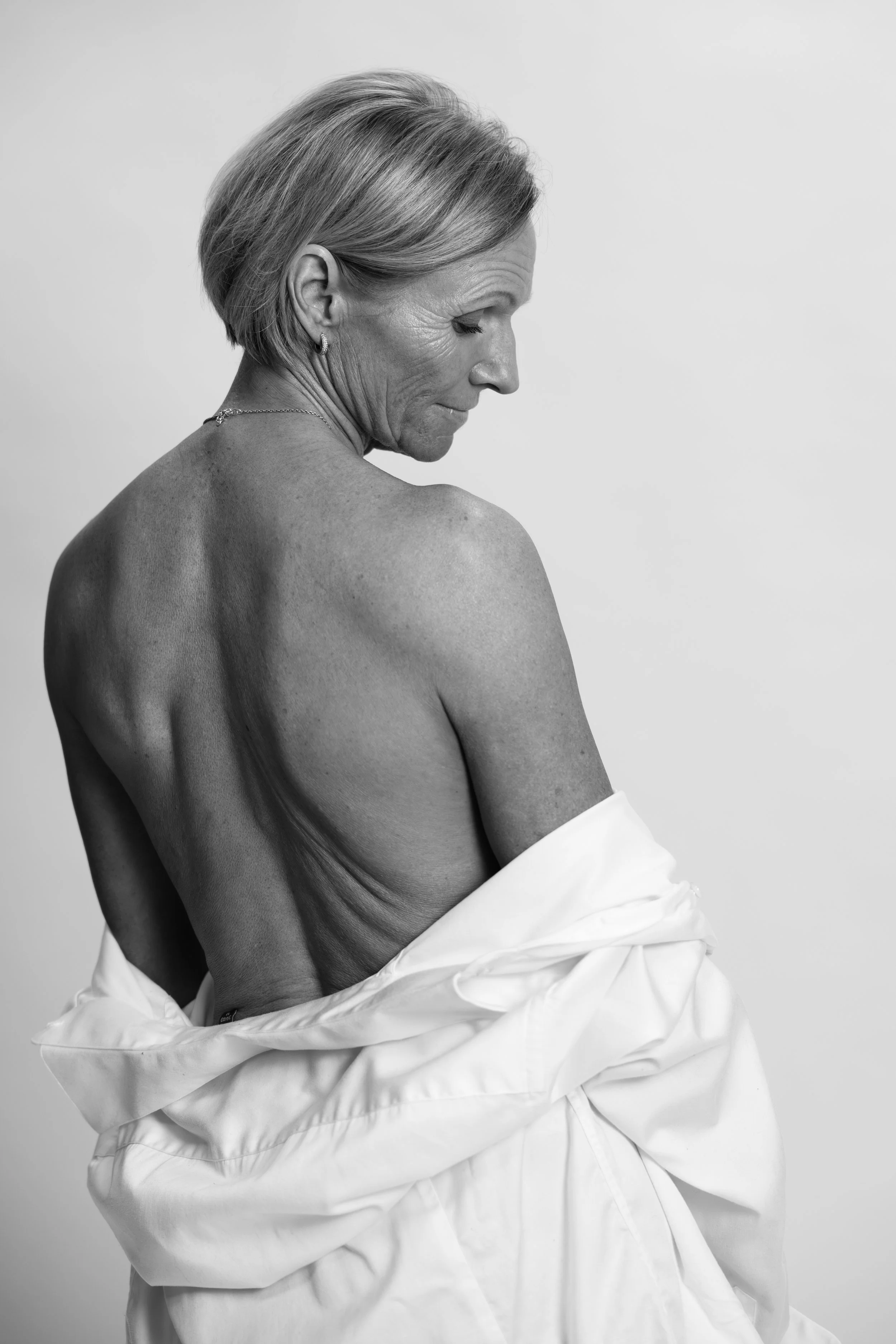 Svart-kvitt-fotografi av ei eldre kvinne med kort, lyst hår, sett i profil og iført ein kvit kjole mot ein nøytral bakgrunn.