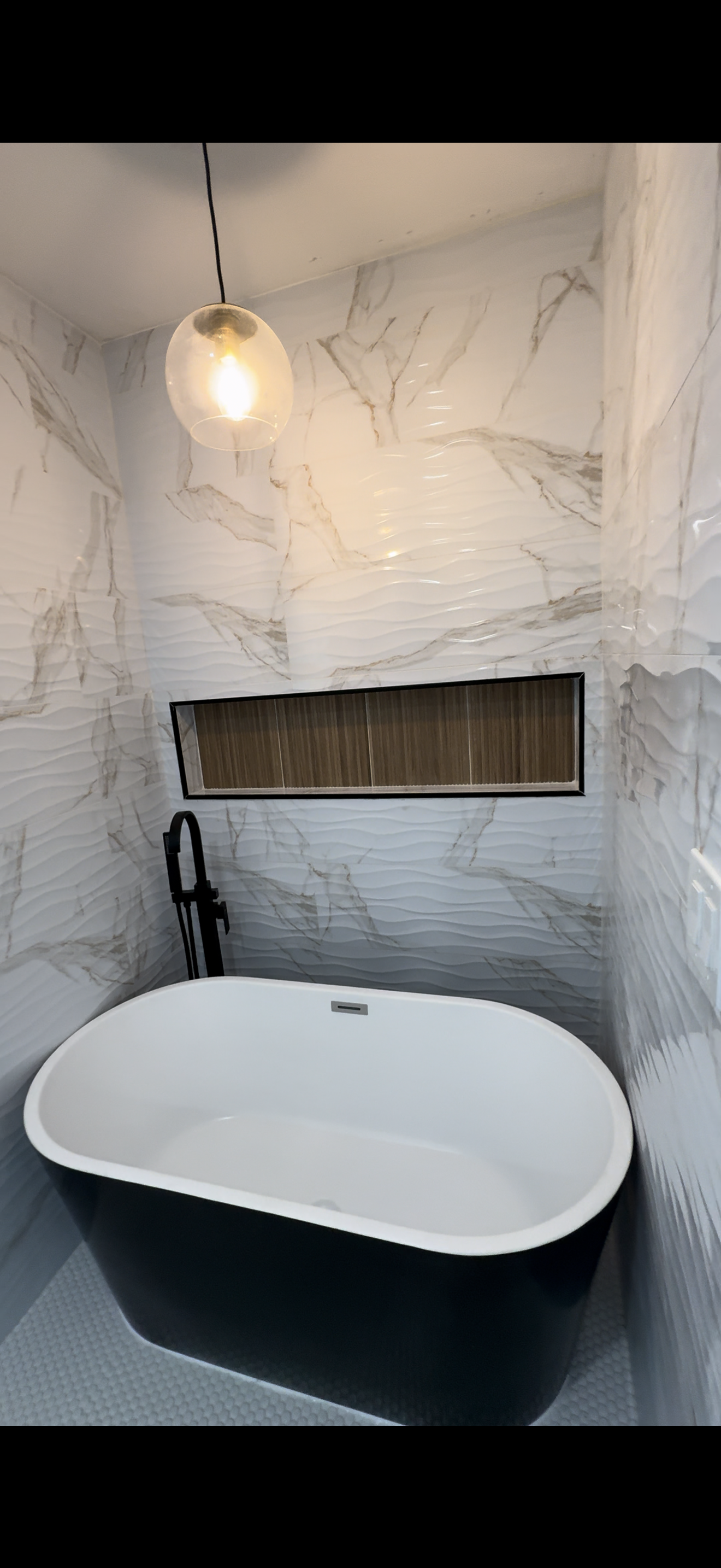 Modern bathroom with a black bathtub, textured white marble wall, black faucet, and a spherical ceiling light.