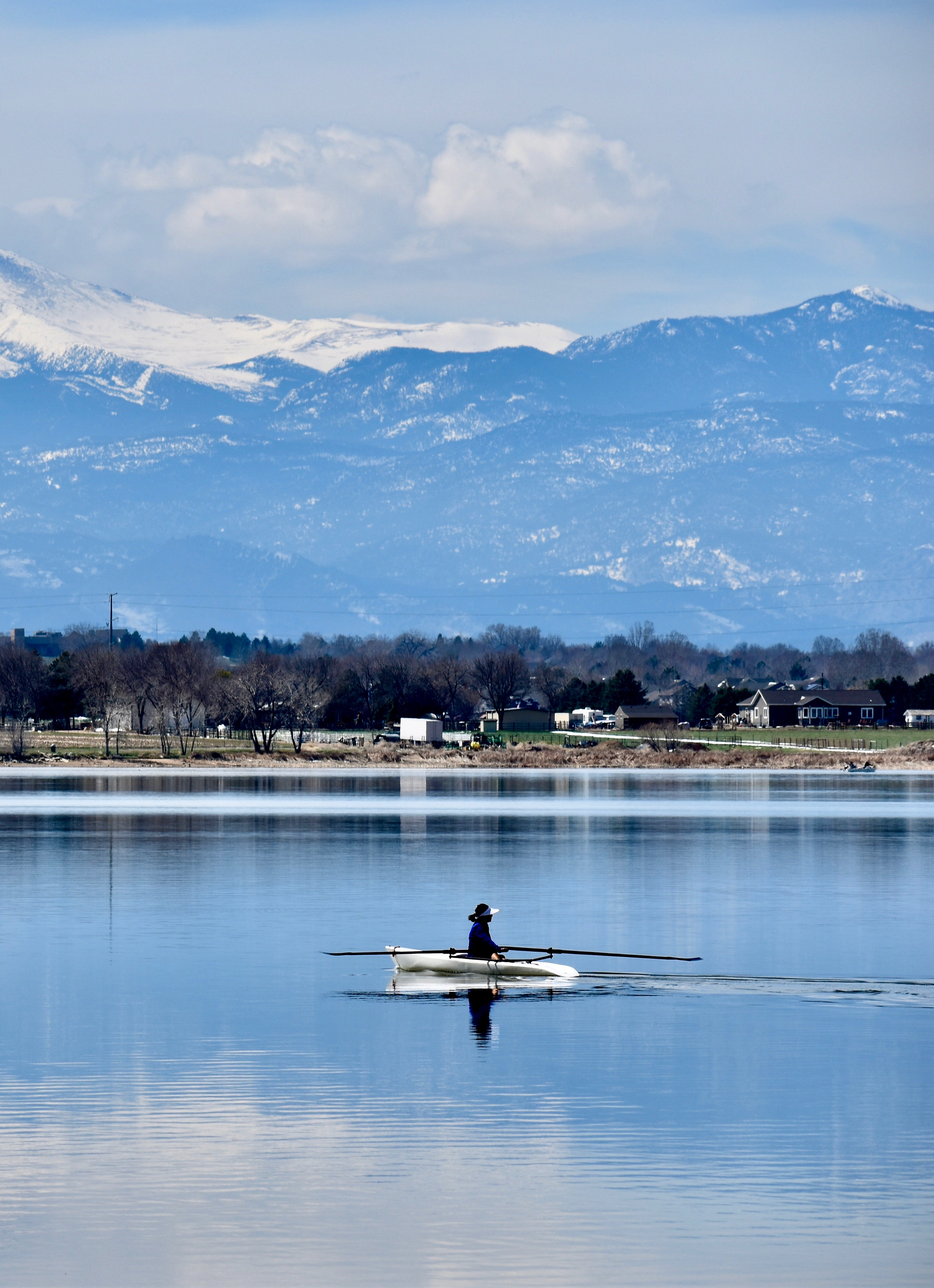 Person kayaking on a calm lake with mountains and cloudy sky in the background.