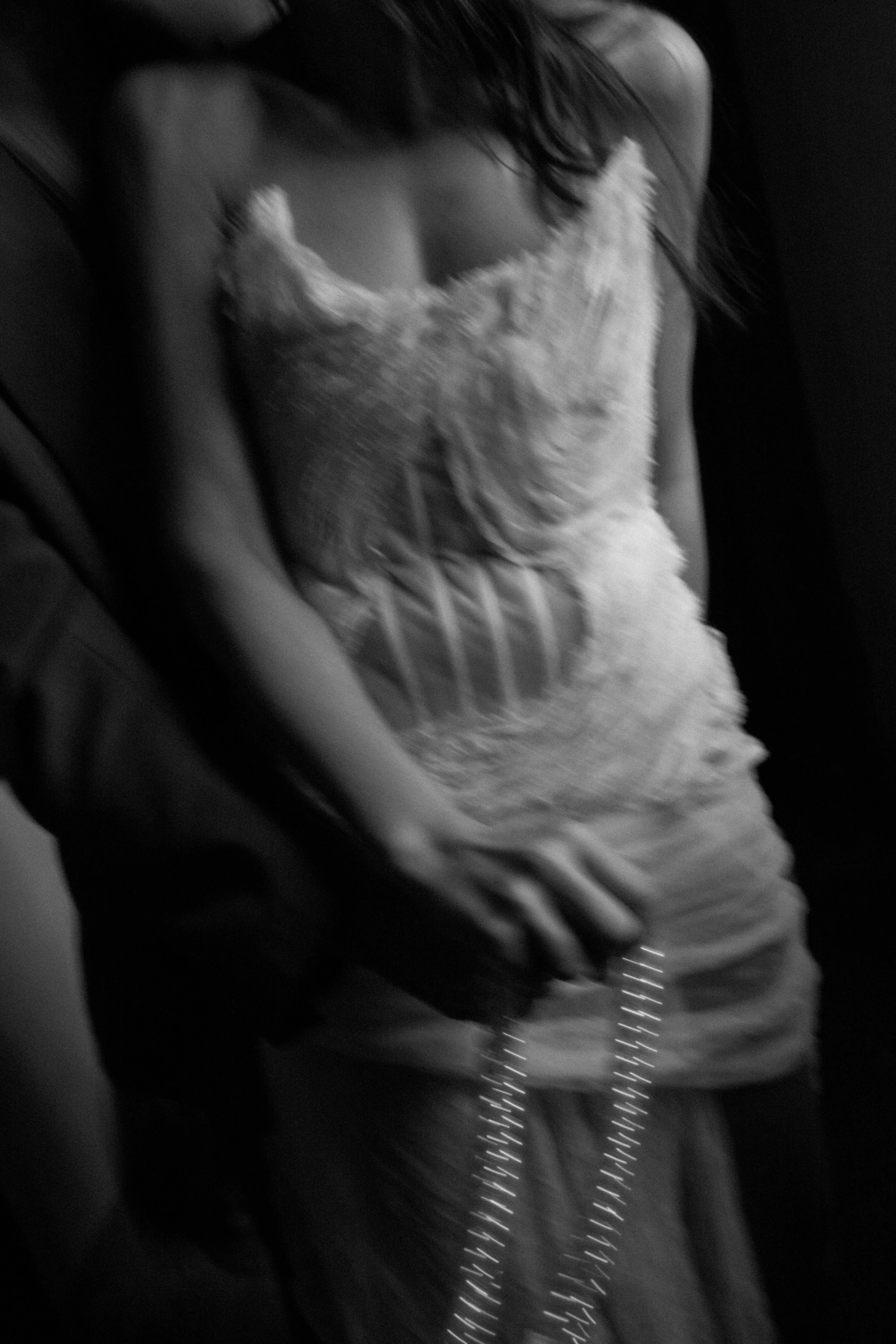 Black and white photo of a woman wearing a lace slip dress with a plunging neckline, sitting on a surface with her hands resting on her lap.