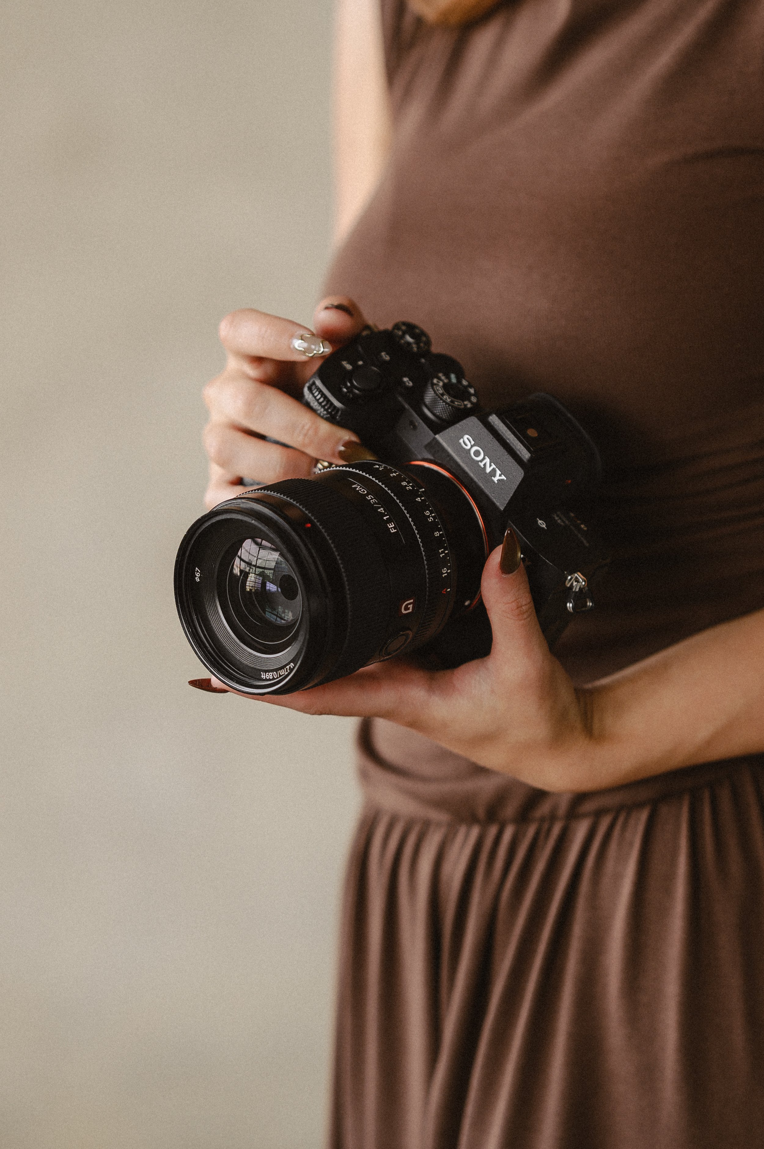 A person wearing a brown dress holding a Sony camera with a large lens.