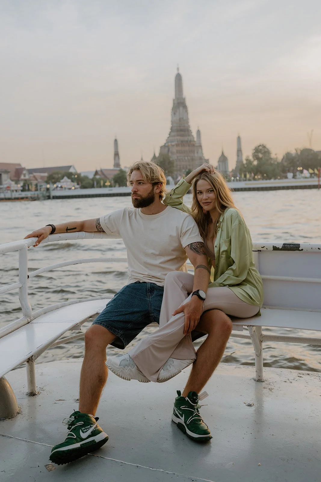 A couple sitting on a boat with a temple in the background, likely in Bangkok.