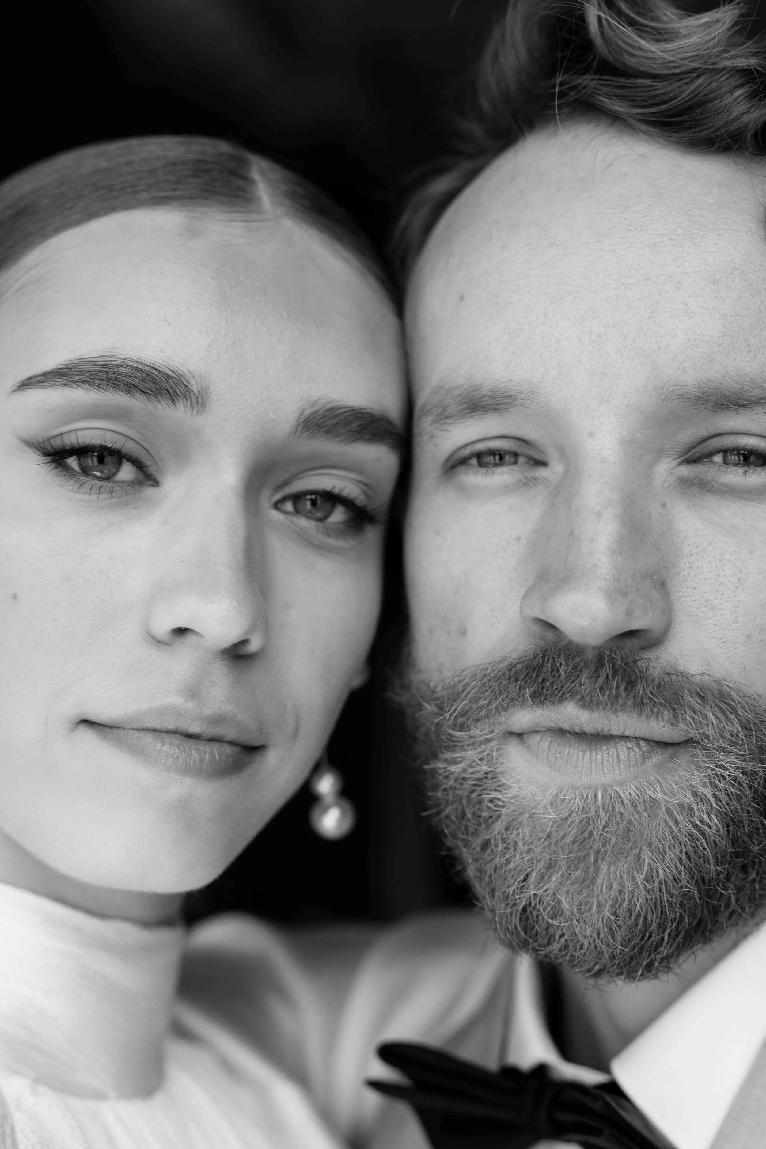 Close-up black and white photo of a young woman and a man lying down with their faces close together, both looking at the camera.