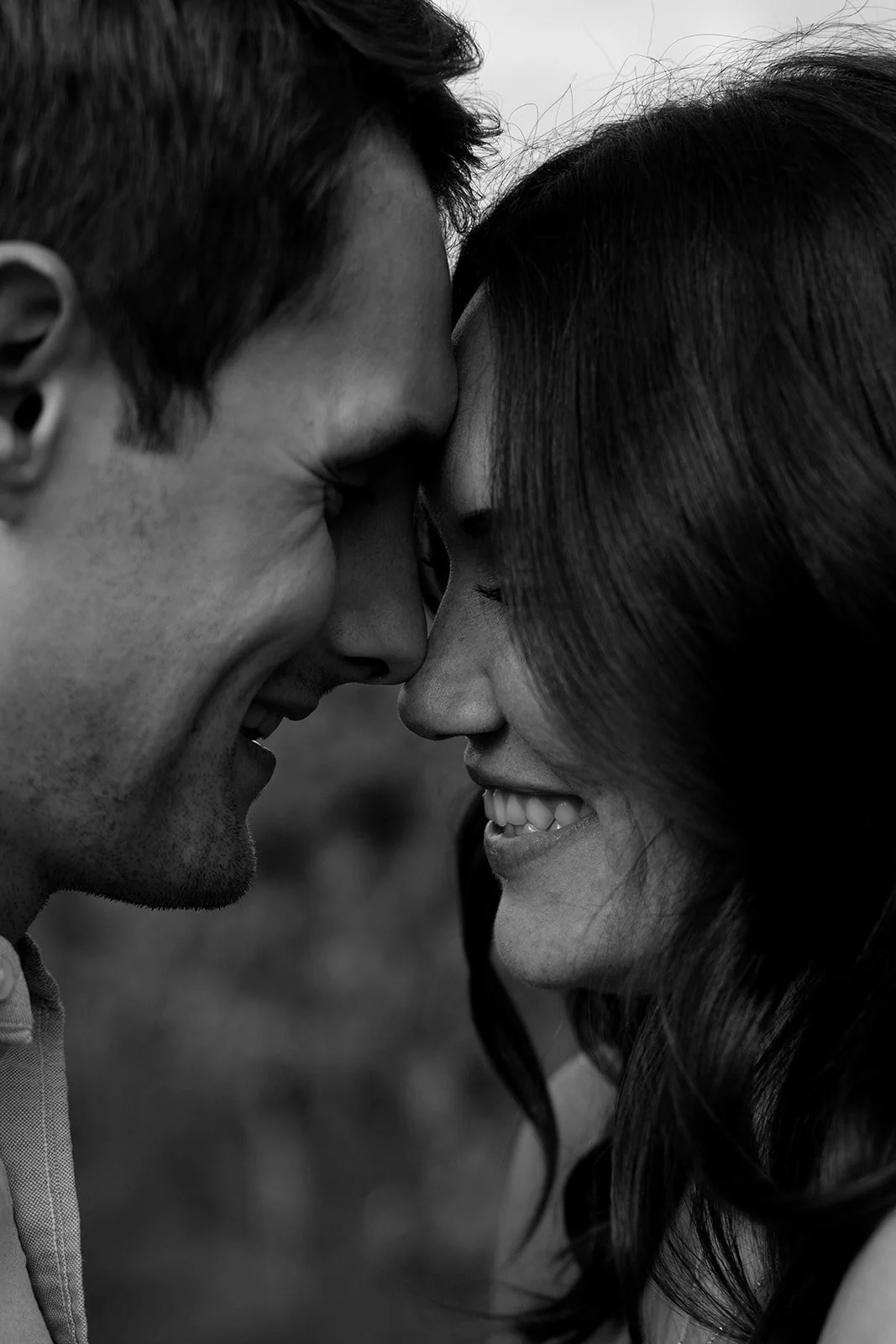 Close-up black and white photograph of a smiling couple with their foreheads touching, eyes closed.