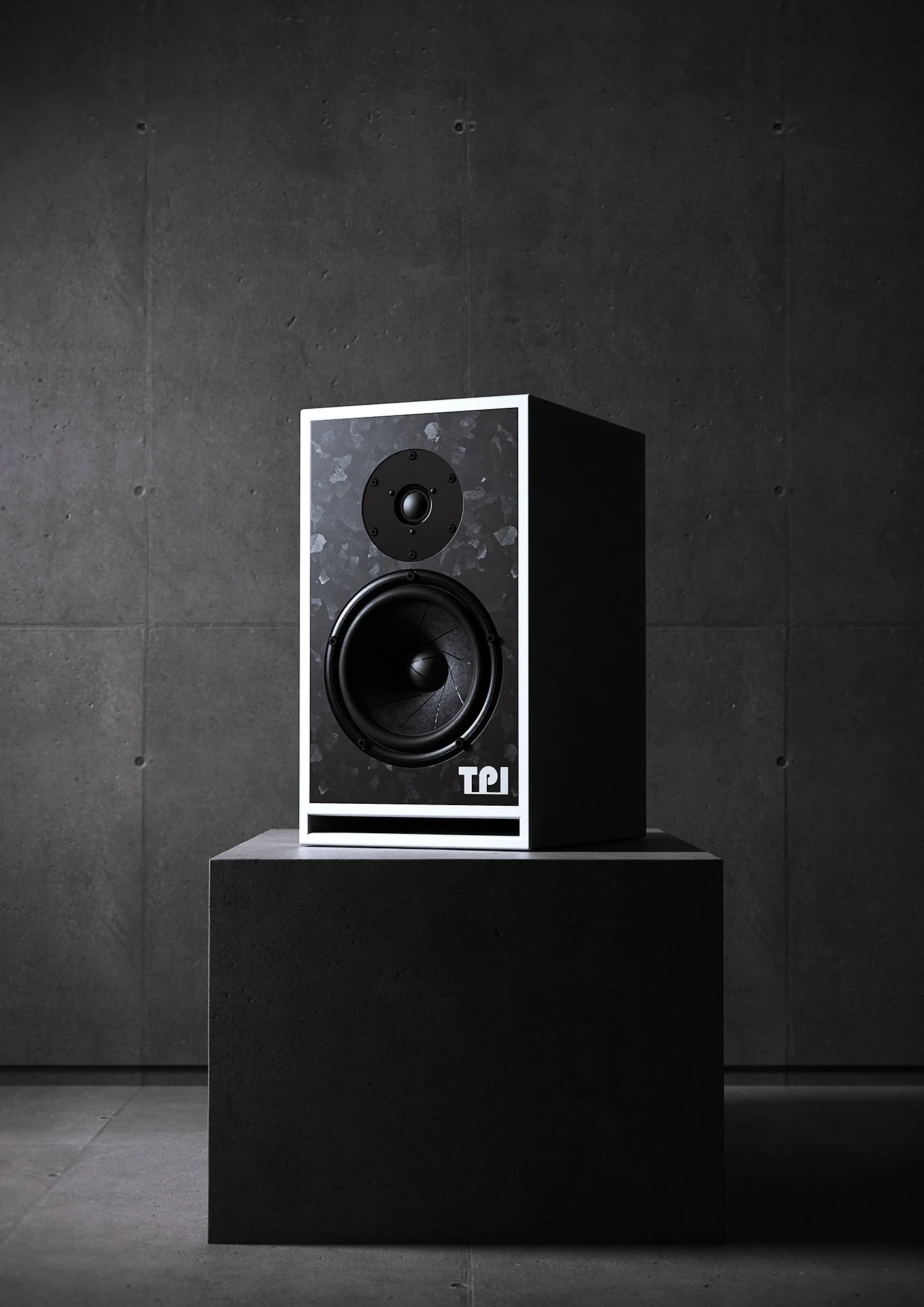 A black and white speaker on a concrete pedestal against a dark textured wall.