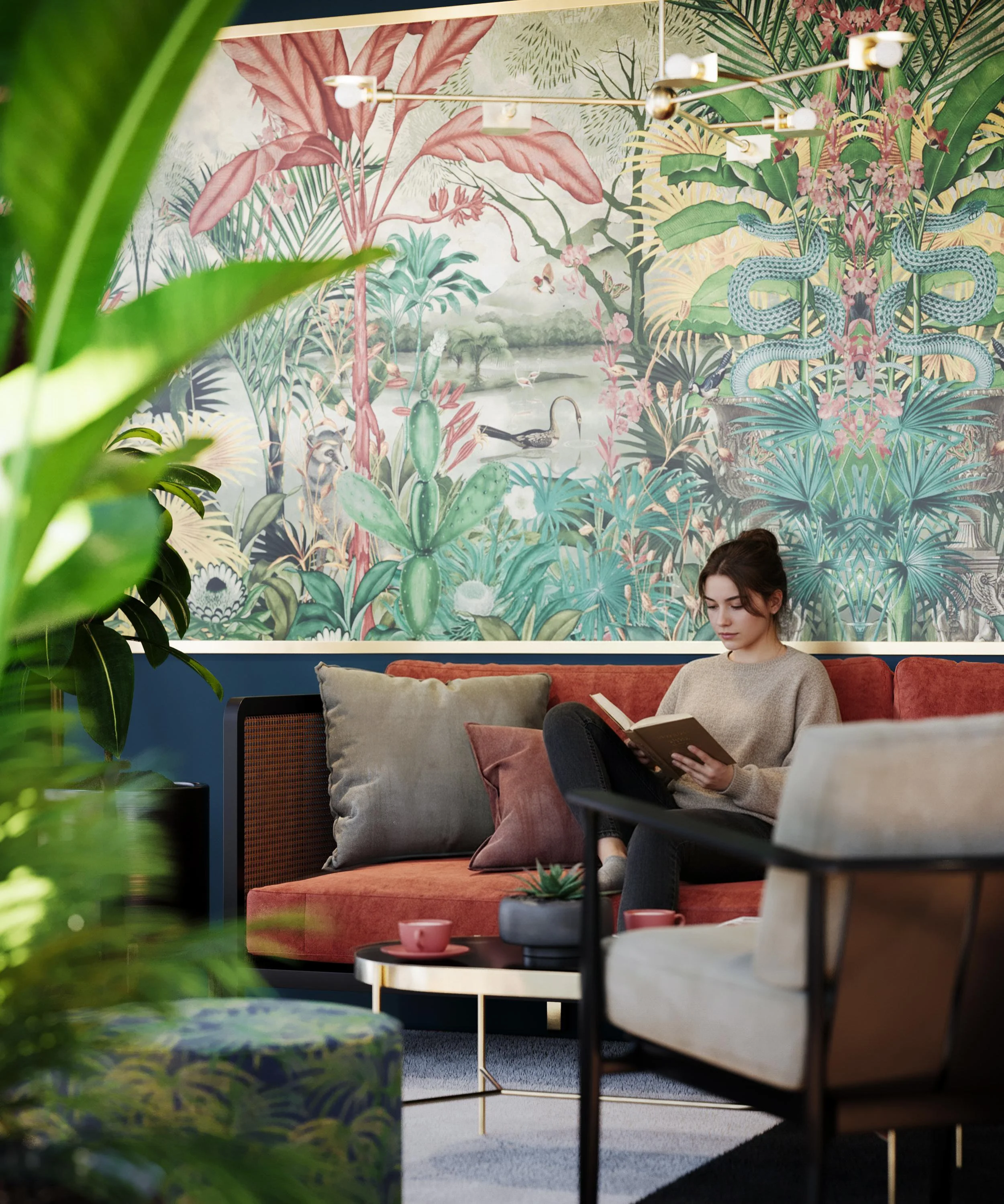 A young woman with brown hair sitting on a pink couch and reading a book in a room decorated with a large jungle-themed mural featuring various plants, trees, flowers, and a waterfowl. The scene is partially obscured by green plants in the foreground