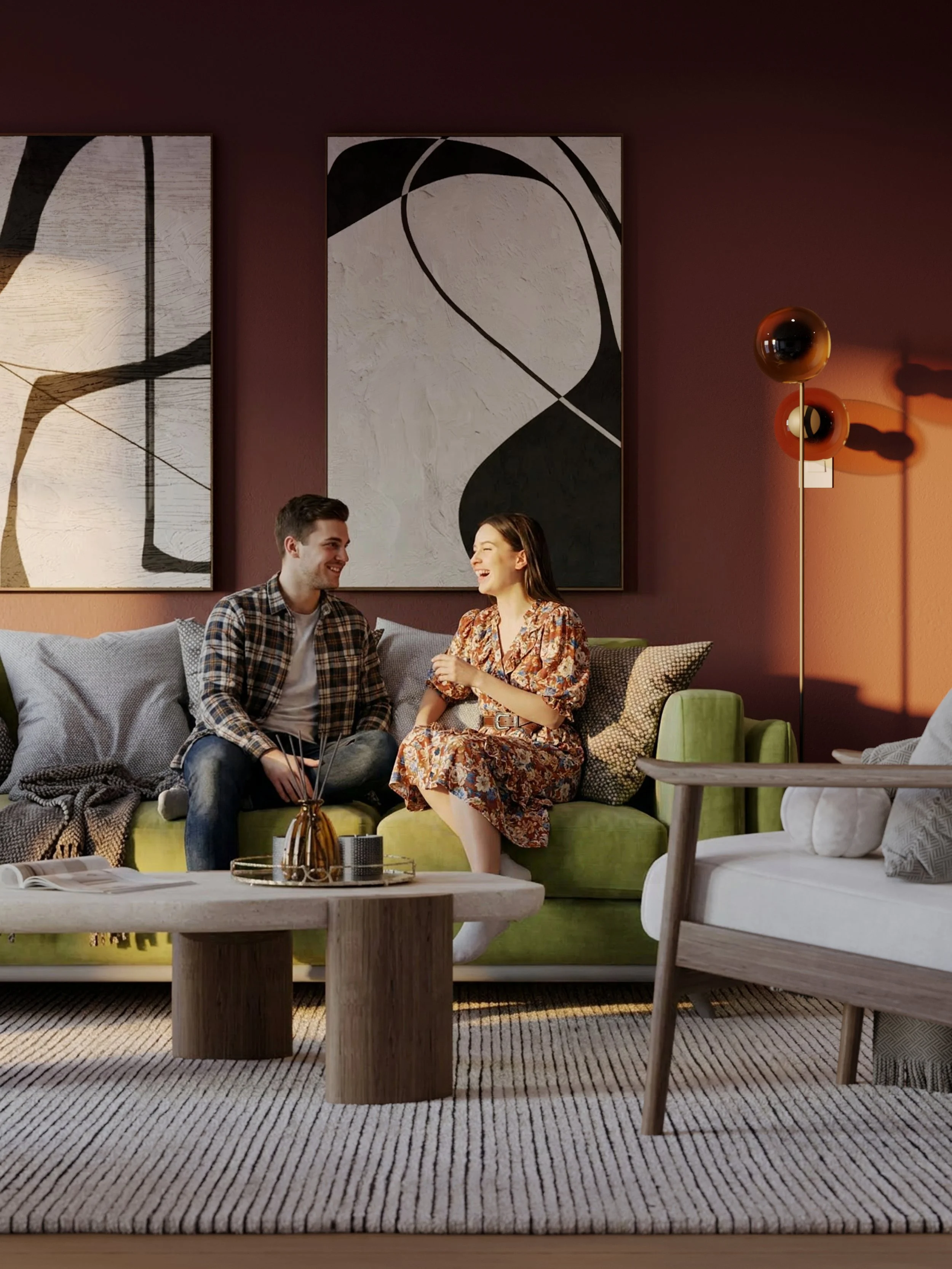 Two people sitting on a green sofa in a living room, smiling and talking. Behind them are three large black and white abstract paintings on a dark red wall, with a floor lamp casting shadows. A wooden coffee table with a decorative item and magazines