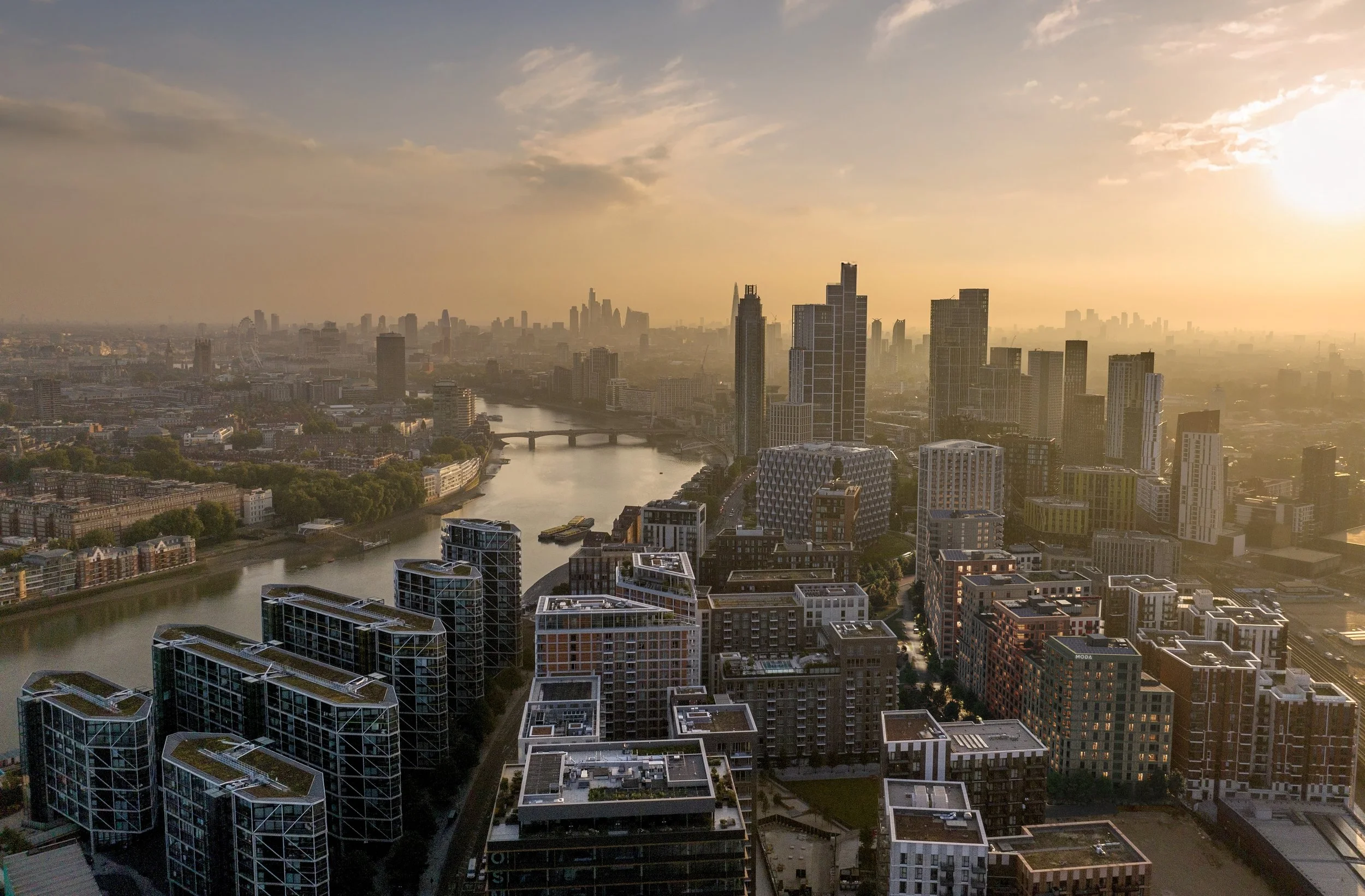 City skyline at sunset with tall modern buildings and a river flowing through the city.