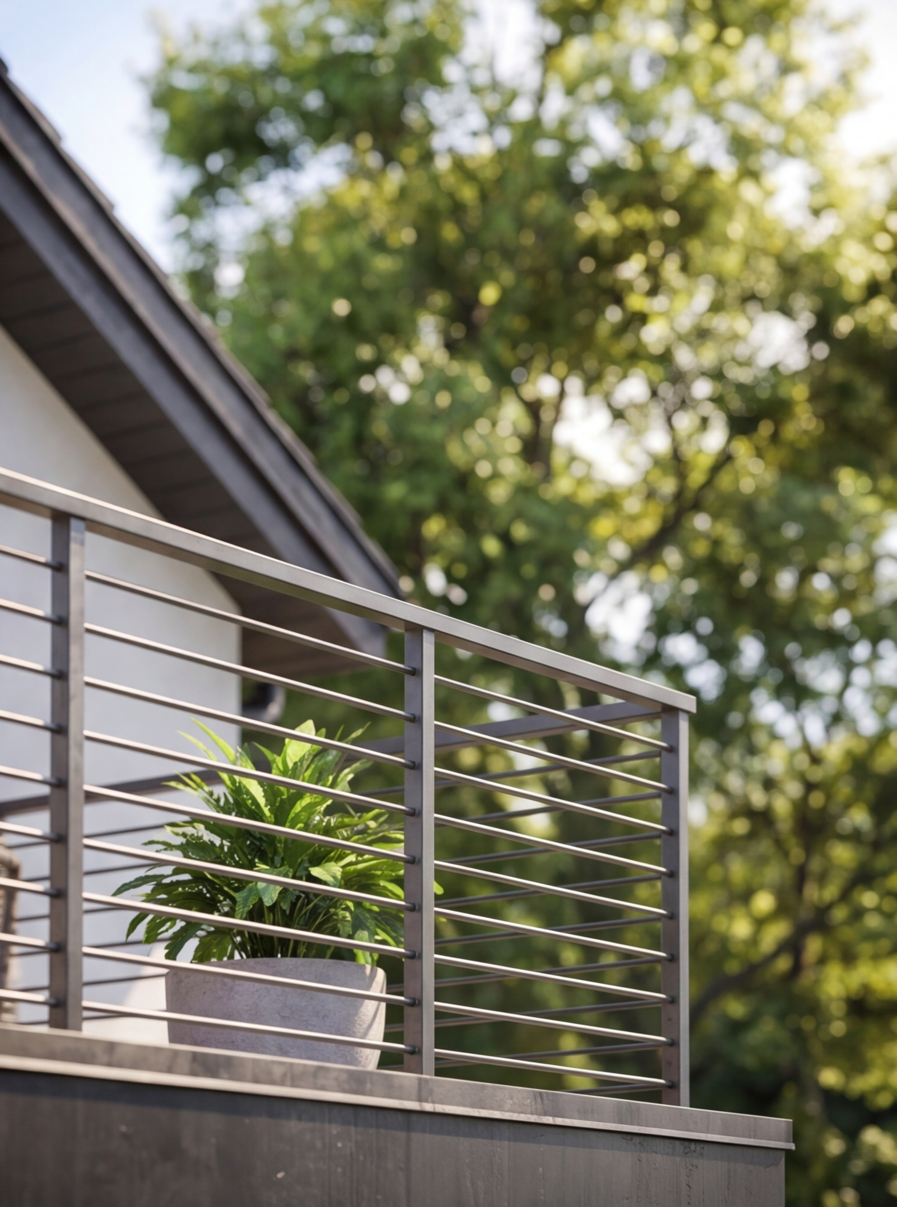 A potted green plant on a balcony with a metal railing, with a background of out-of-focus trees and sunlight.