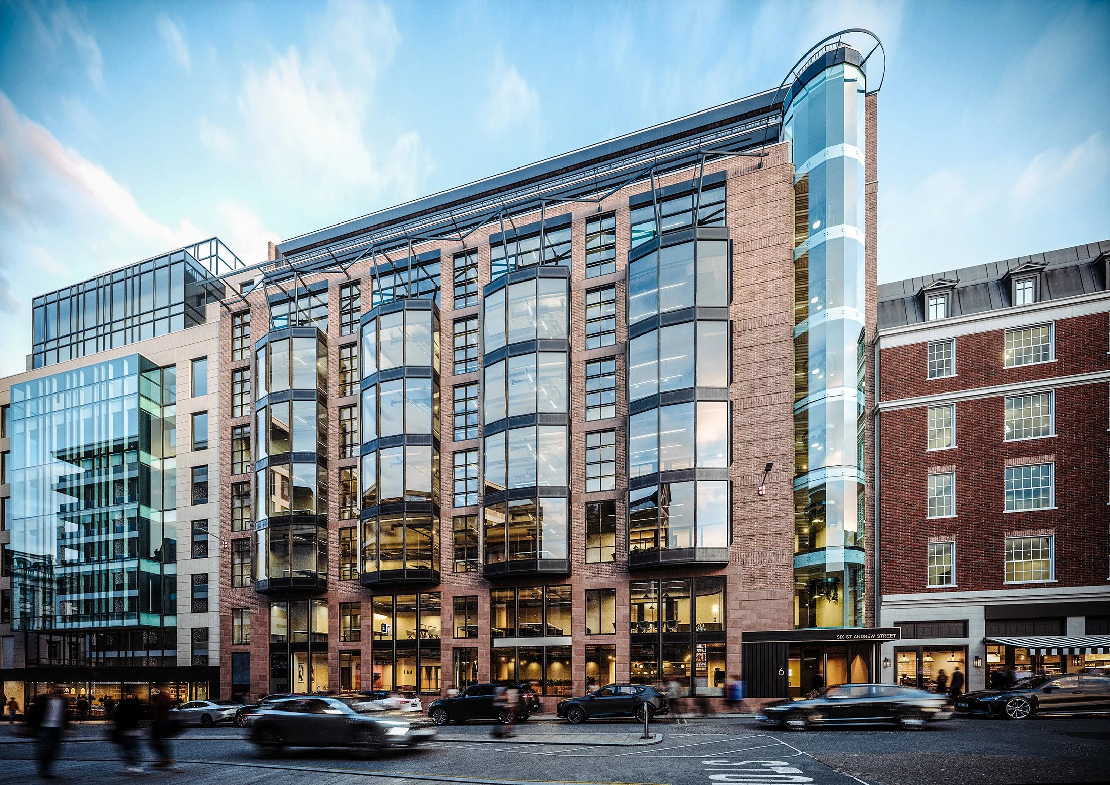 Modern multi-story building with glass windows and brick facade, located on a city street with cars and people passing by