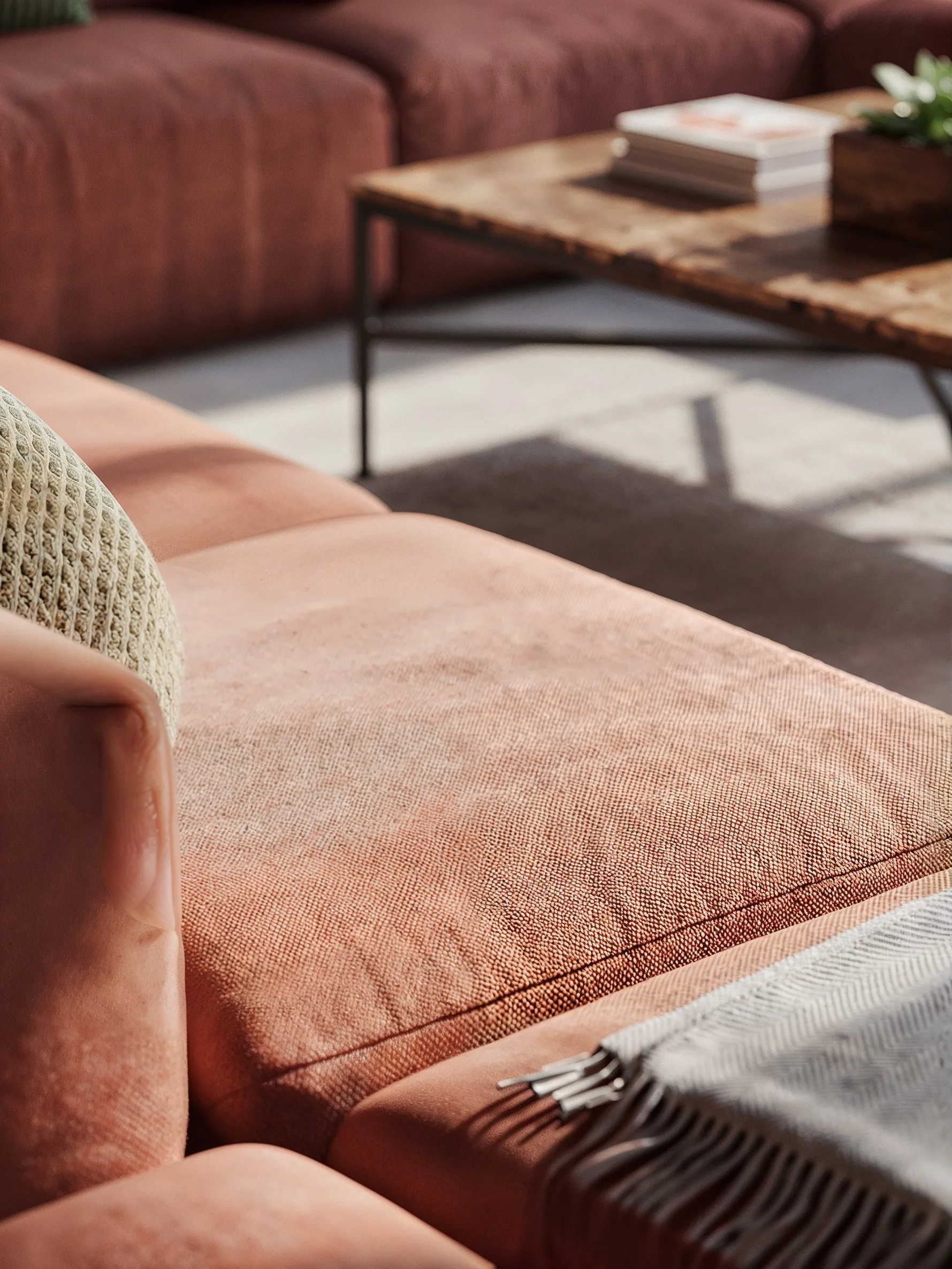 Close-up of a pink upholstered sofa and a wooden coffee table with magazines and decorative plants in a living room.