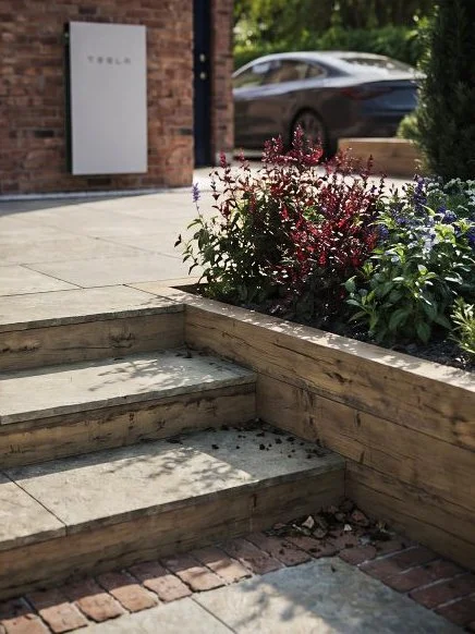 Outdoor sidewalk with flower bed and stairs, Tesla sign on brick wall, blurred car in background.