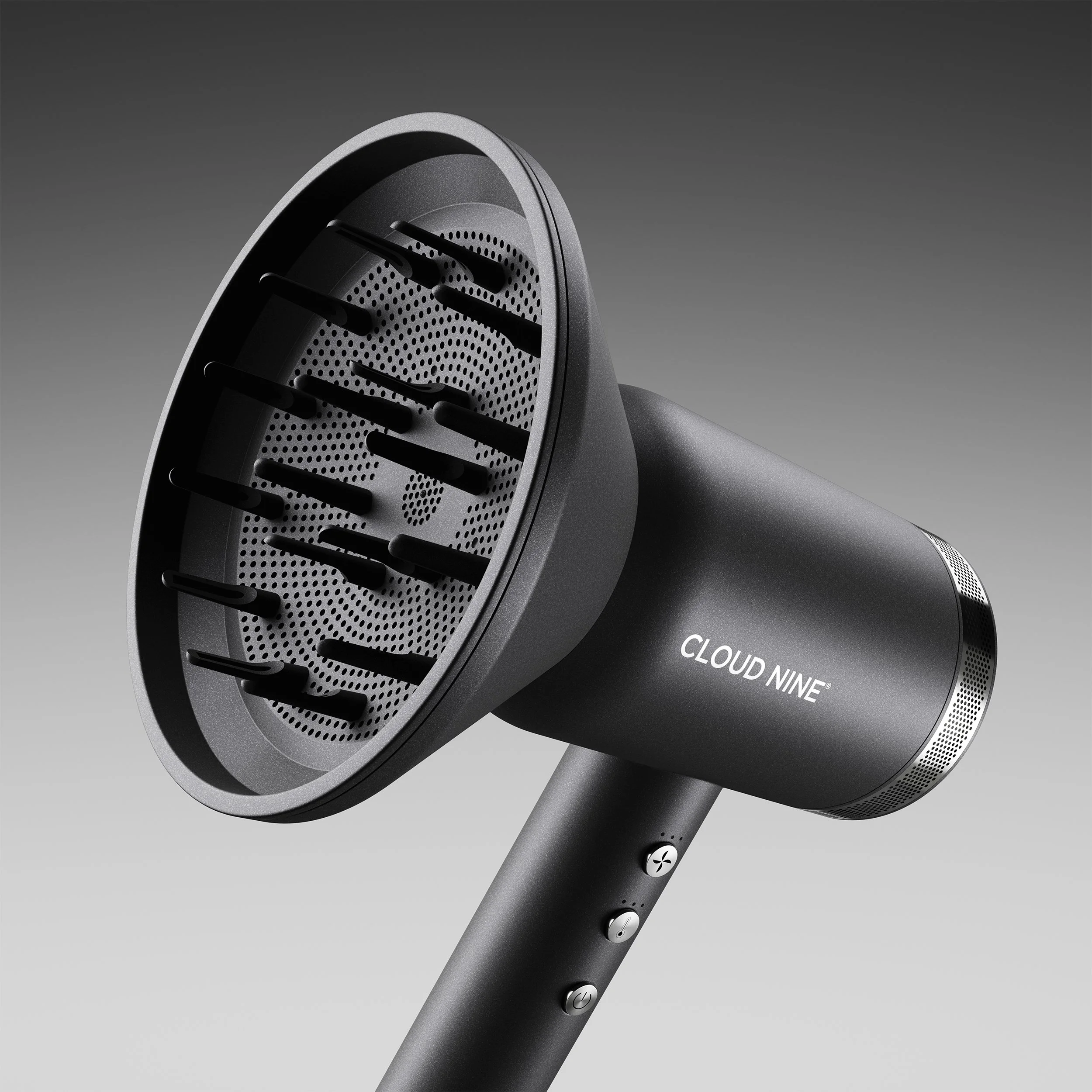 Close-up of a modern, sleek electric hair dryer with a matte black finish, featuring a perforated air intake and control buttons on its handle, set against a plain gray background.