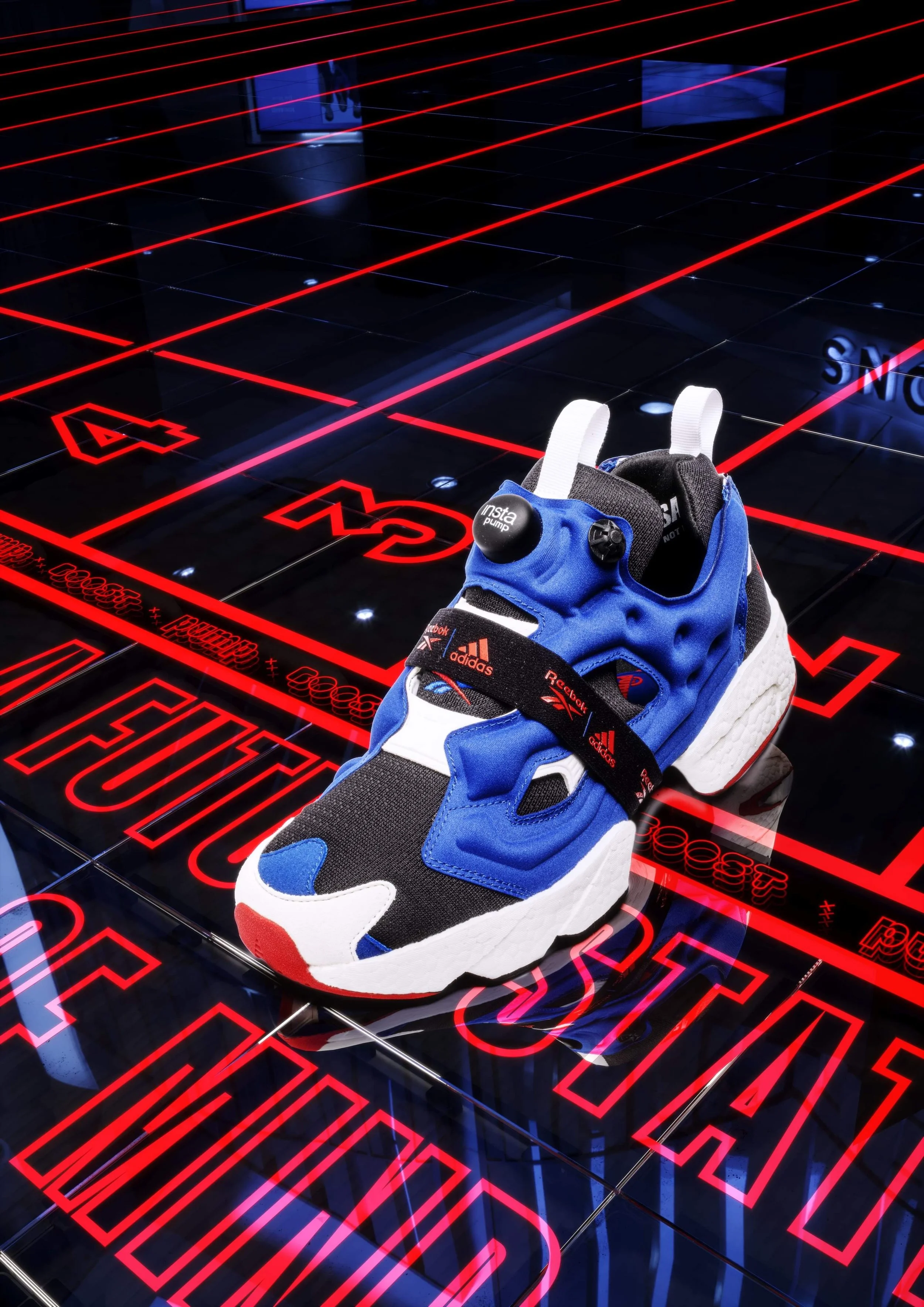 A blue, black, and white Reebok sneaker with a black InstaPump logo, white tongue, and red, white, and blue accents, placed on a black surface with bright red grid lines and illuminated text and icons.