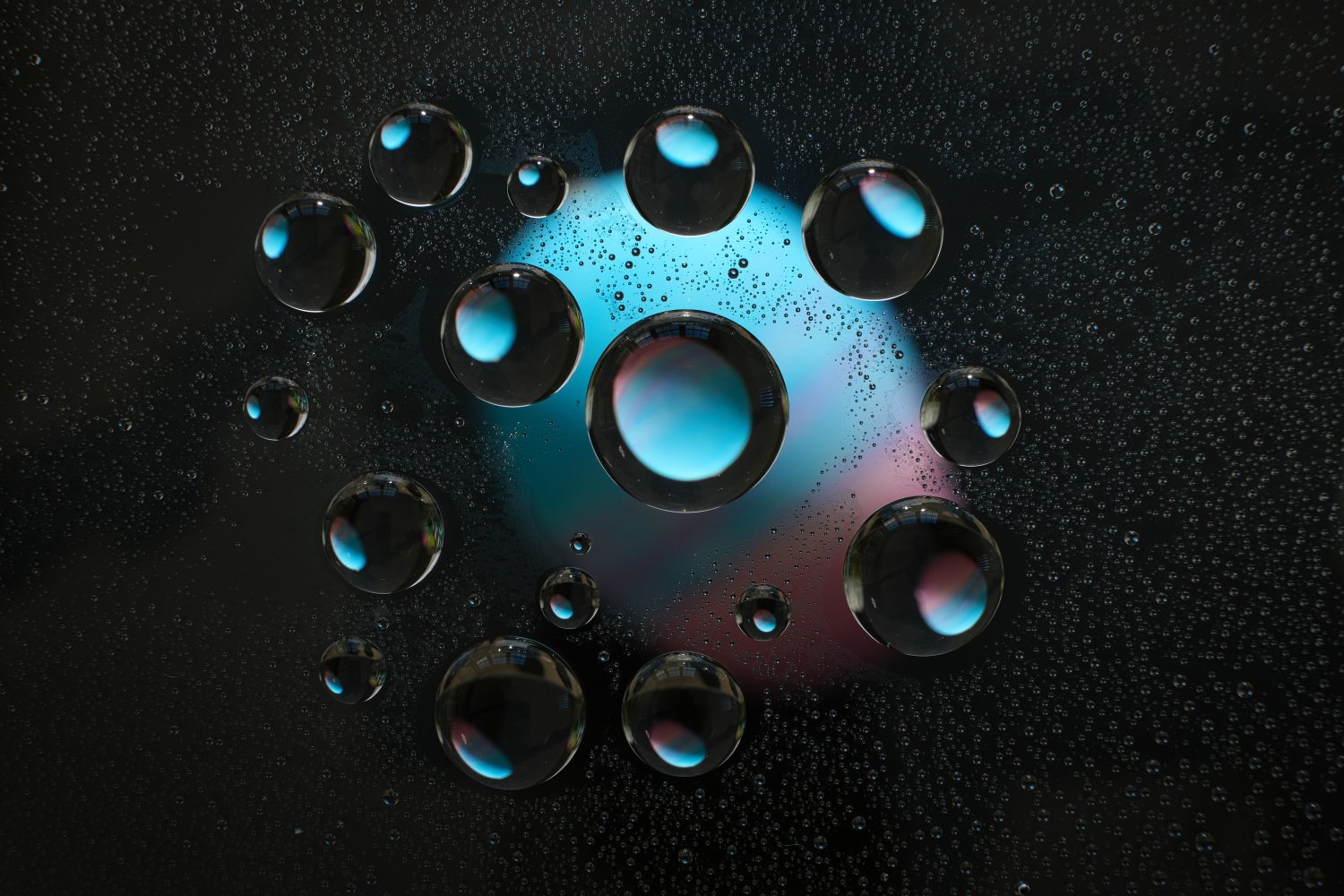 Close-up of water bubbles on a dark surface with a colorful, blurry background.