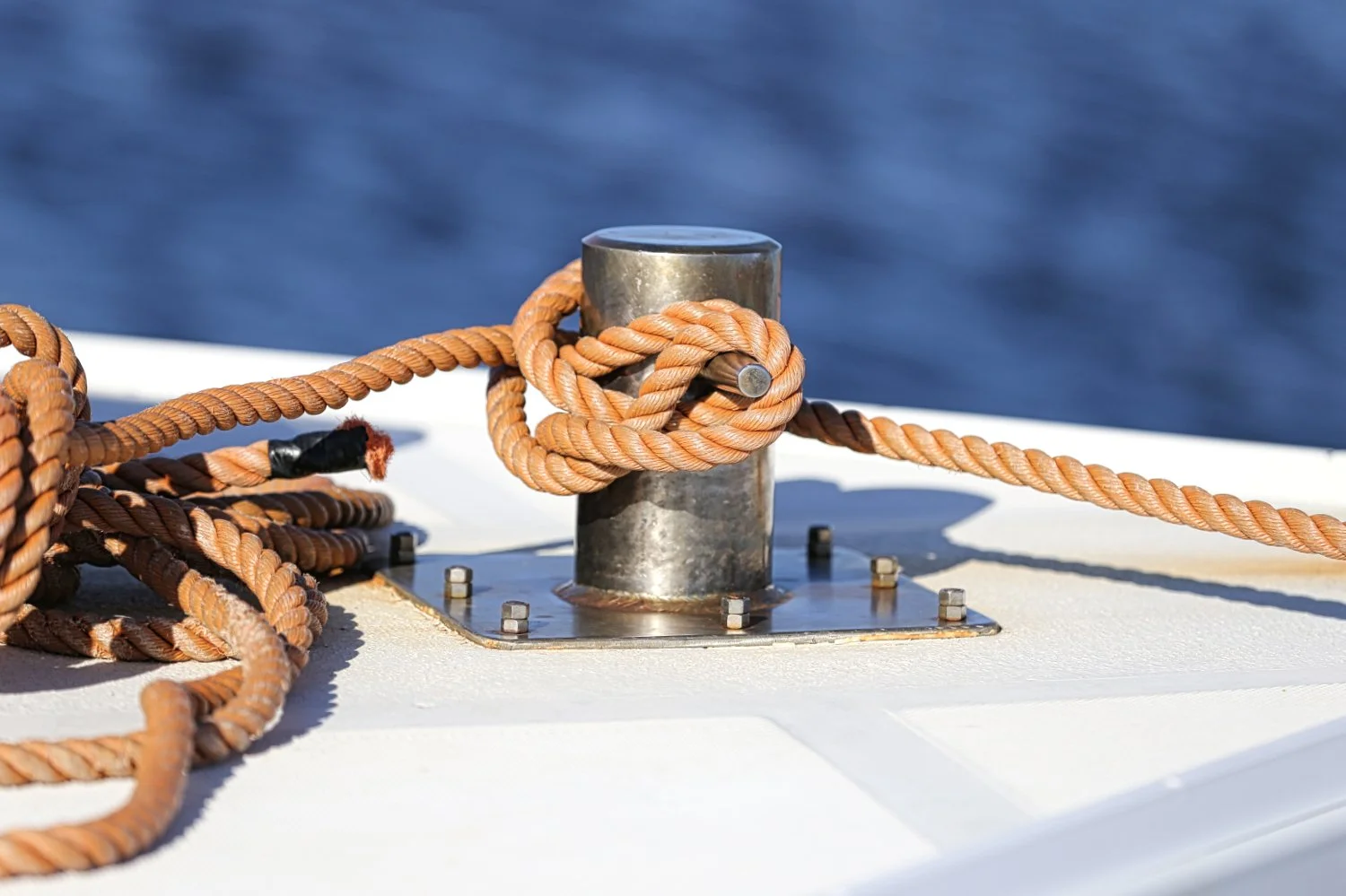 Close-up of a metal mooring point with a knotted orange rope secured to a boat, with blue water in the background.