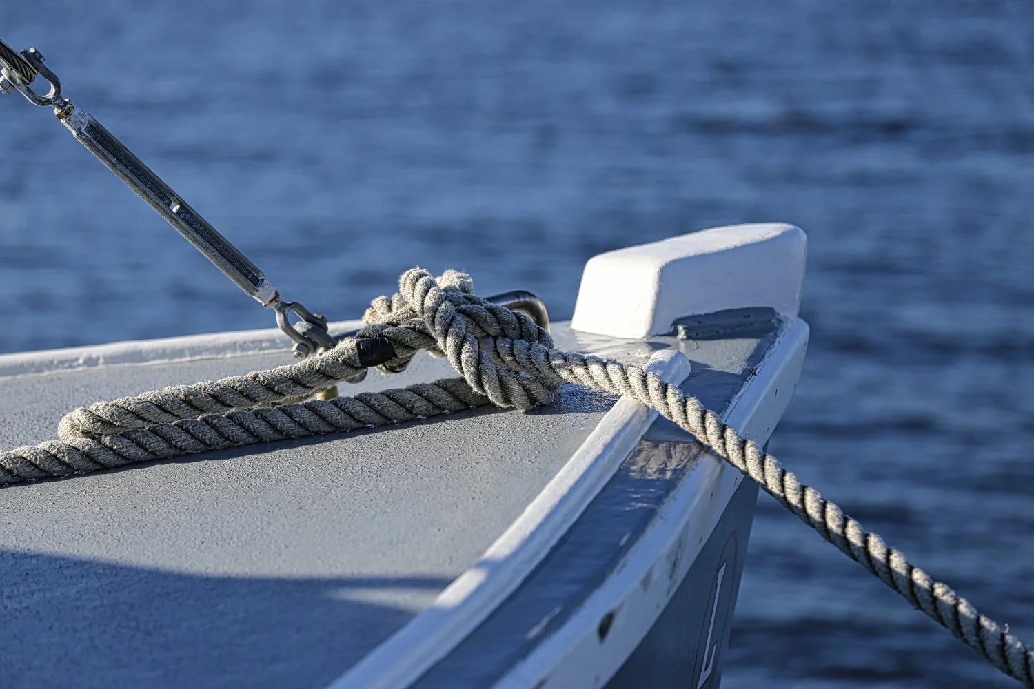 Close-up of a boat's bow with a rope tied to a metal cleat, floating on the water.