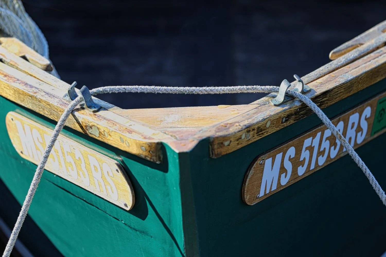 Close-up of a green boat's bow with wooden trim, metal hardware, and a visible registration number MS 51553 RS.