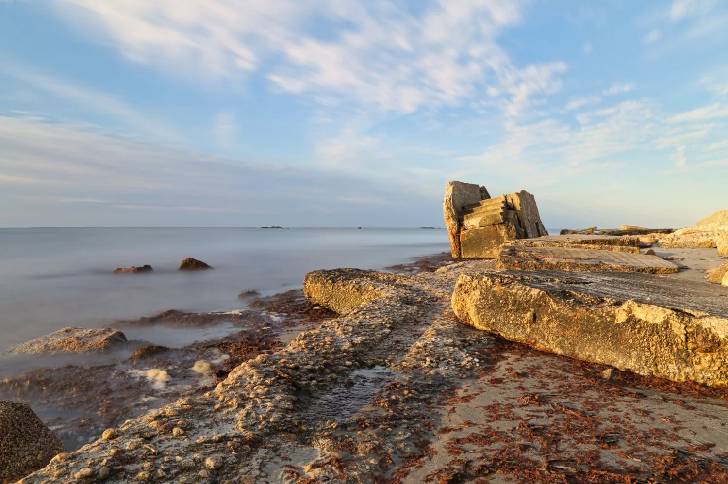 Sunset over rocky beach with calm water and scattered clouds in the sky