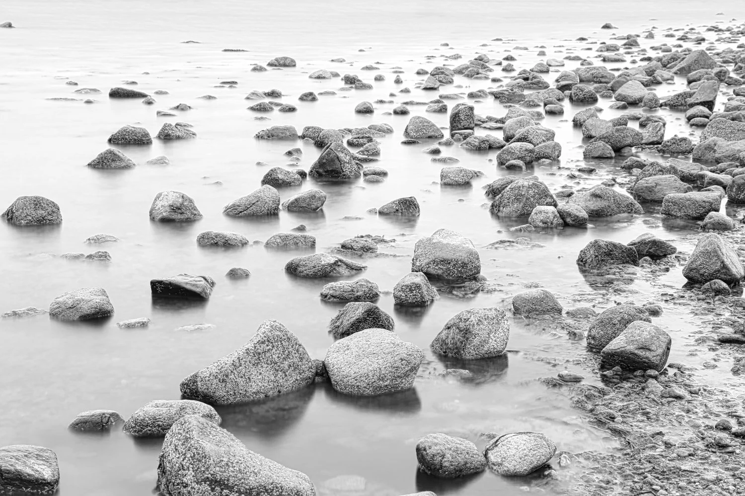 Black and white photo of a rocky shoreline with water surrounding the rocks.