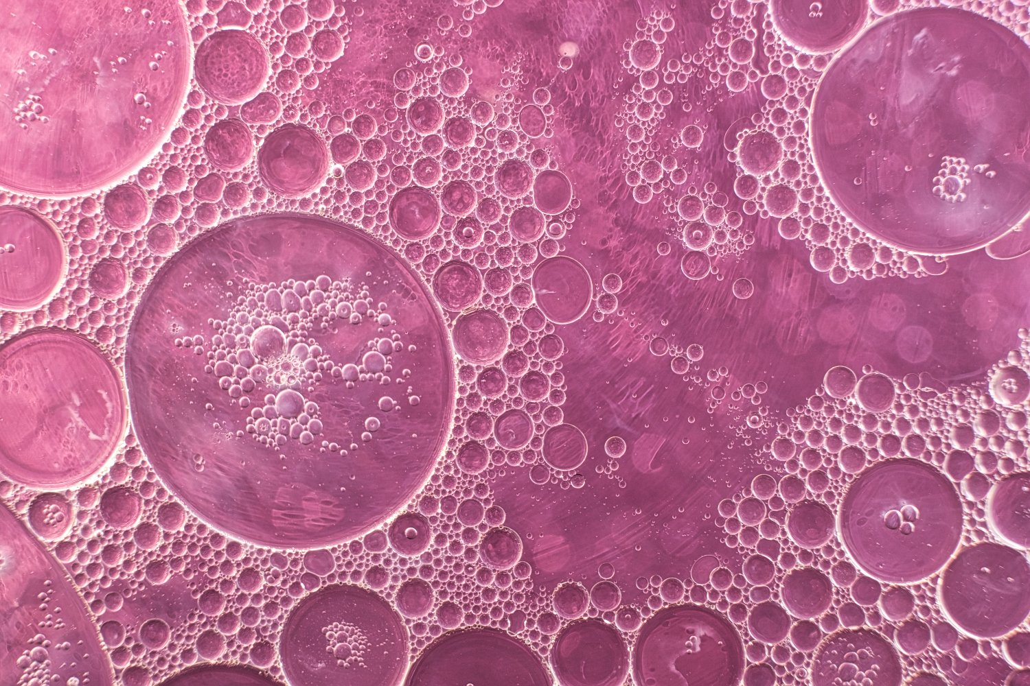 Close-up of pink and purple bubbles of varying sizes in a liquid, creating a textured pattern.