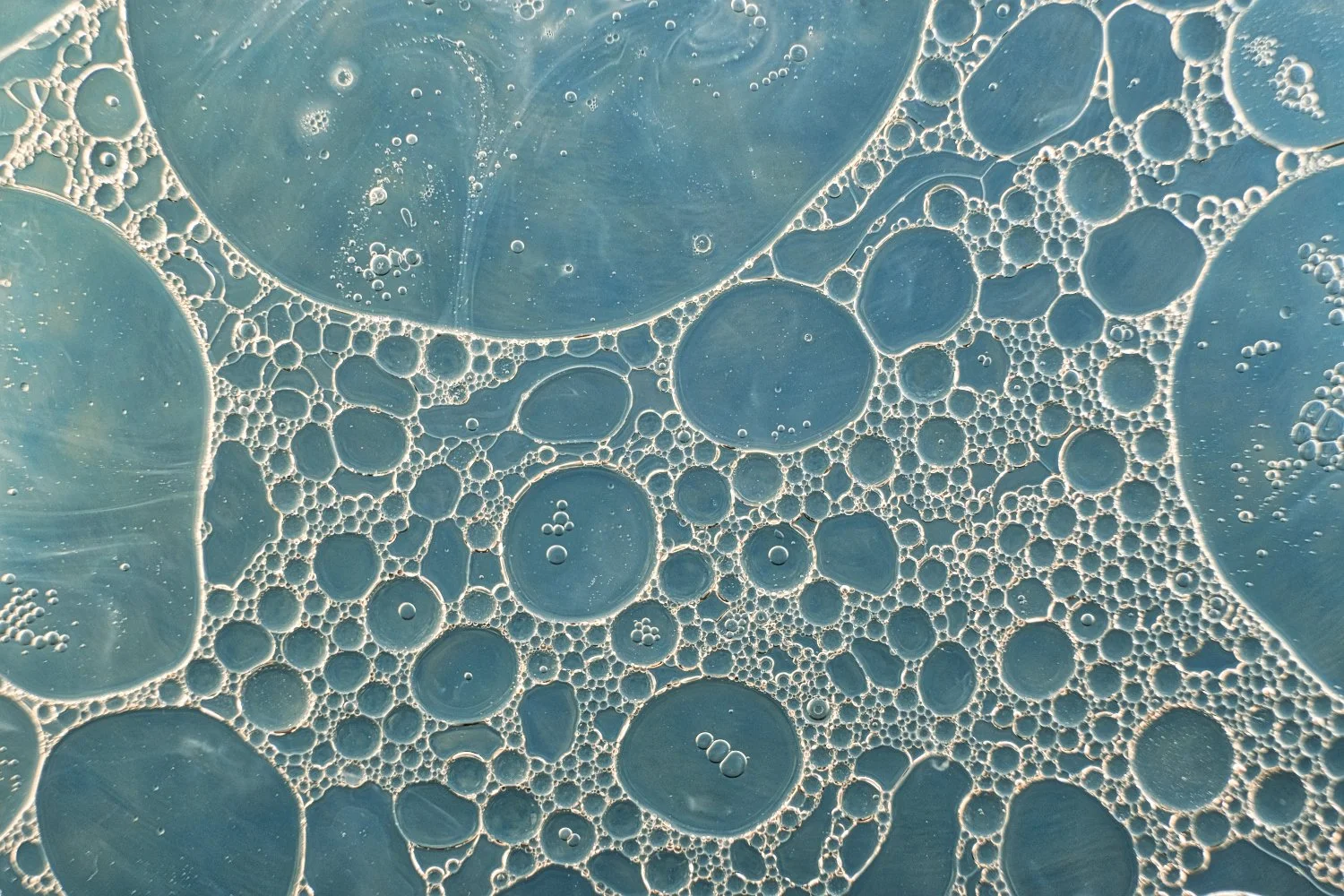 Close-up of soap bubbles in various sizes with blue background visible through them.