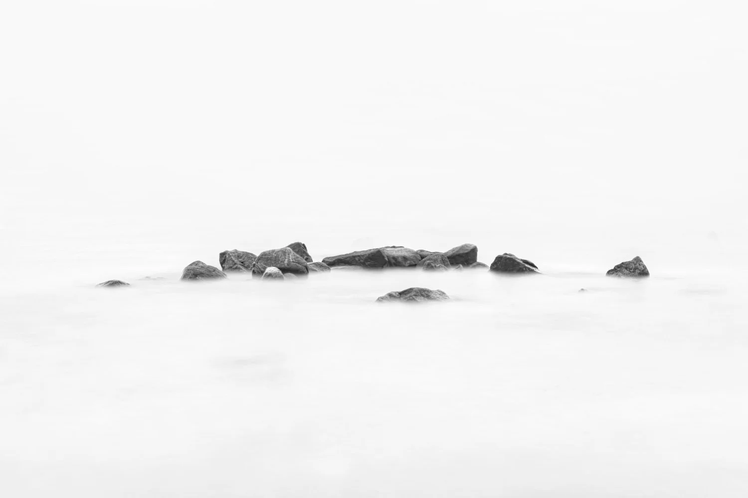 Black and white photo of rocks partially submerged in water, with a blurred and minimalistic background.