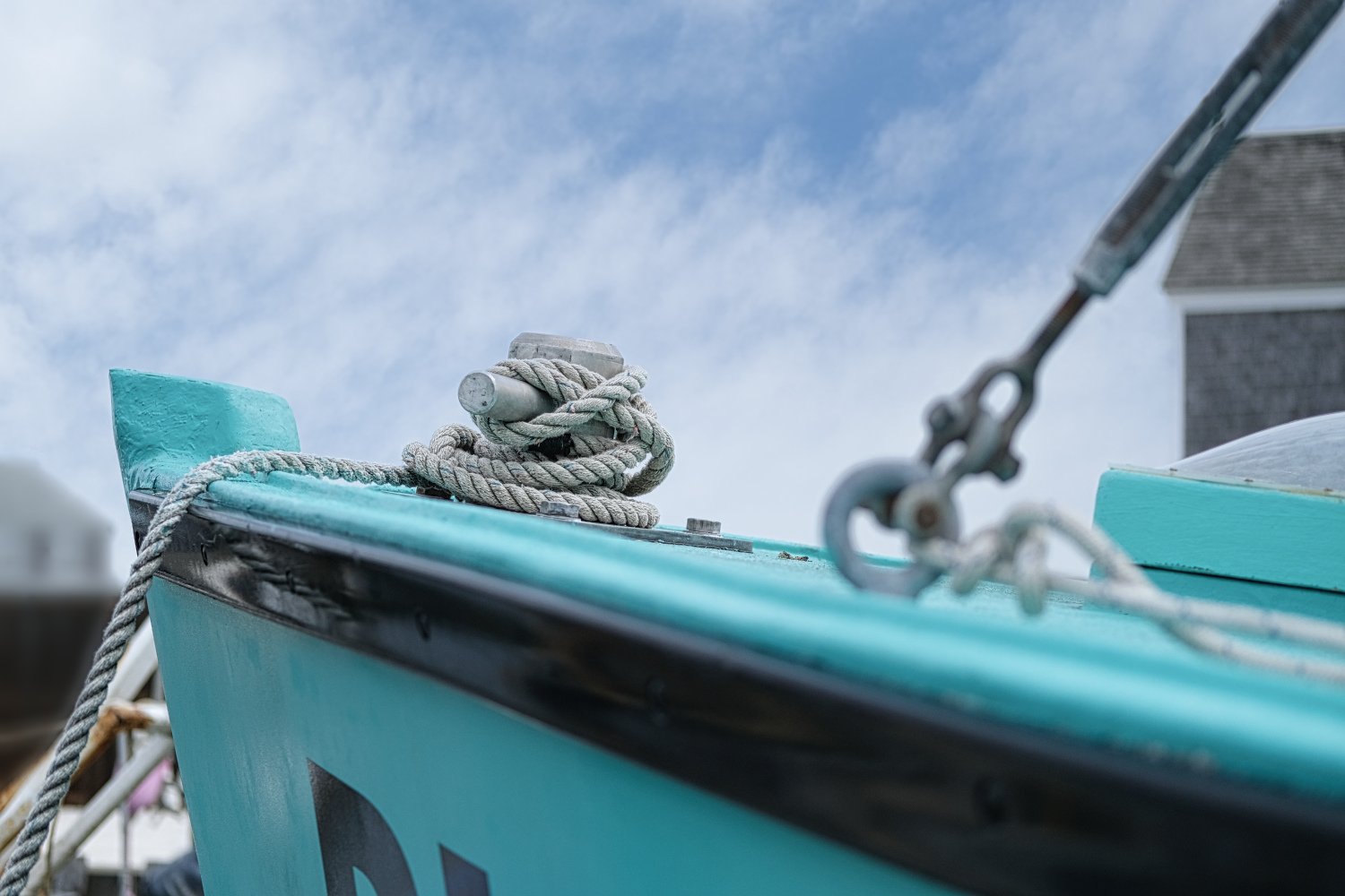 Close-up of a boat's bow with light blue paint, a coiled rope, and metal pulleys attached, with a cloudy sky in the background.
