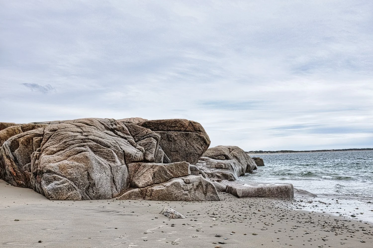 Rock formation on a sandy beach with ocean waves and cloudy sky.