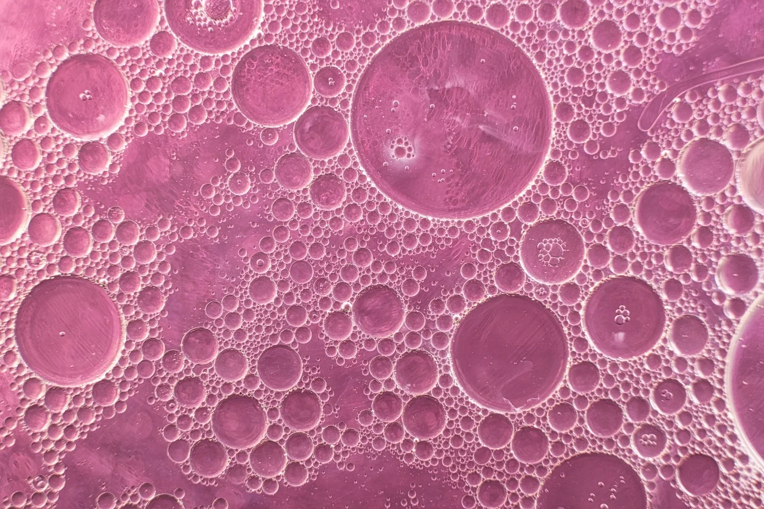 Close-up of pink bubbles and oil droplets, creating a textured pattern.