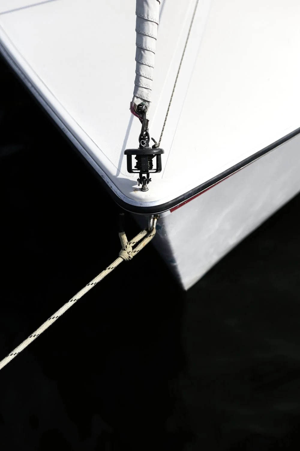 Close-up of the bow of a white sailboat with a sailboat rope, pulley, and winch system to control the sail.