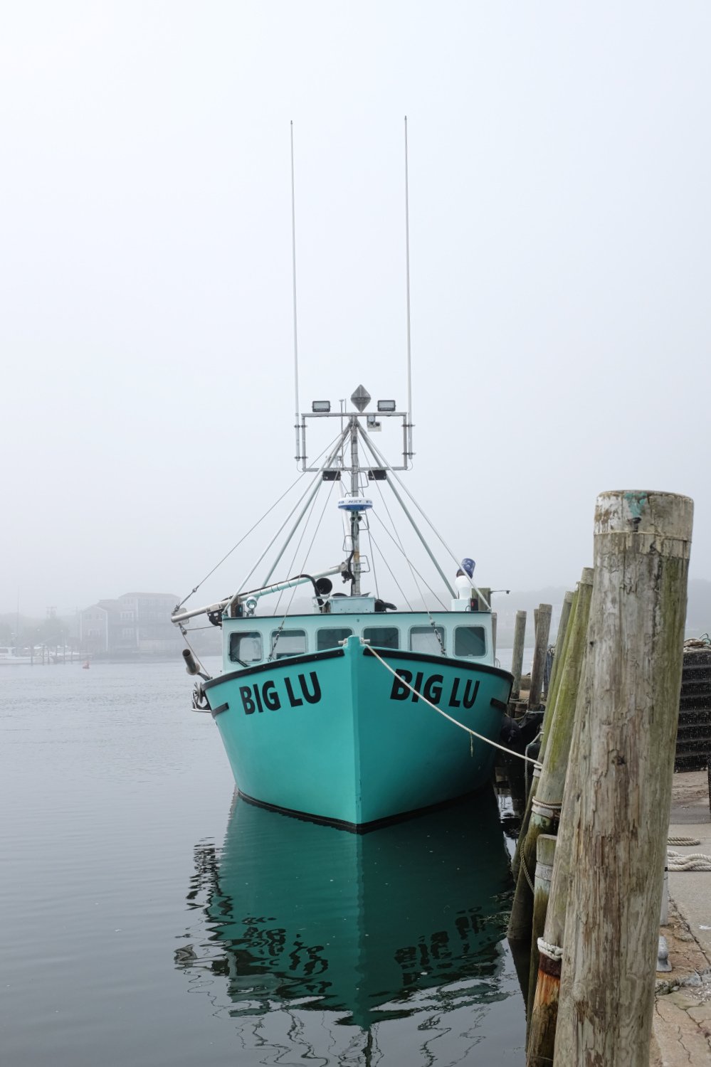 A boat named 'BIG LU' docked at a pier in foggy weather with the water reflecting the vessel.