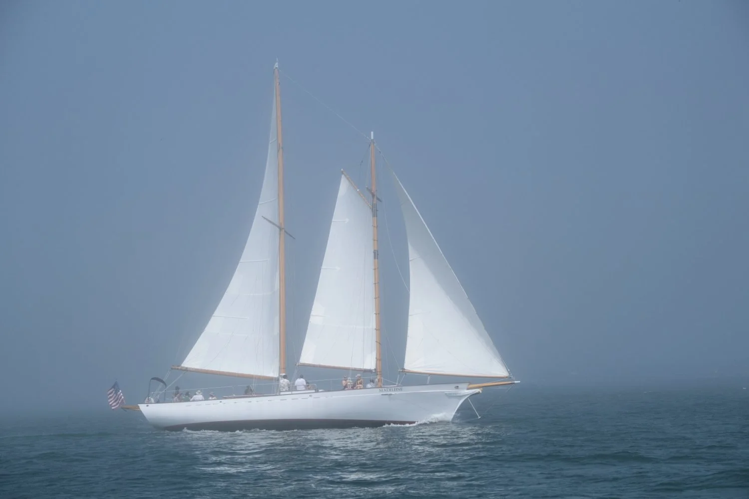 A white sailboat with two masts sailing on calm water in foggy weather.