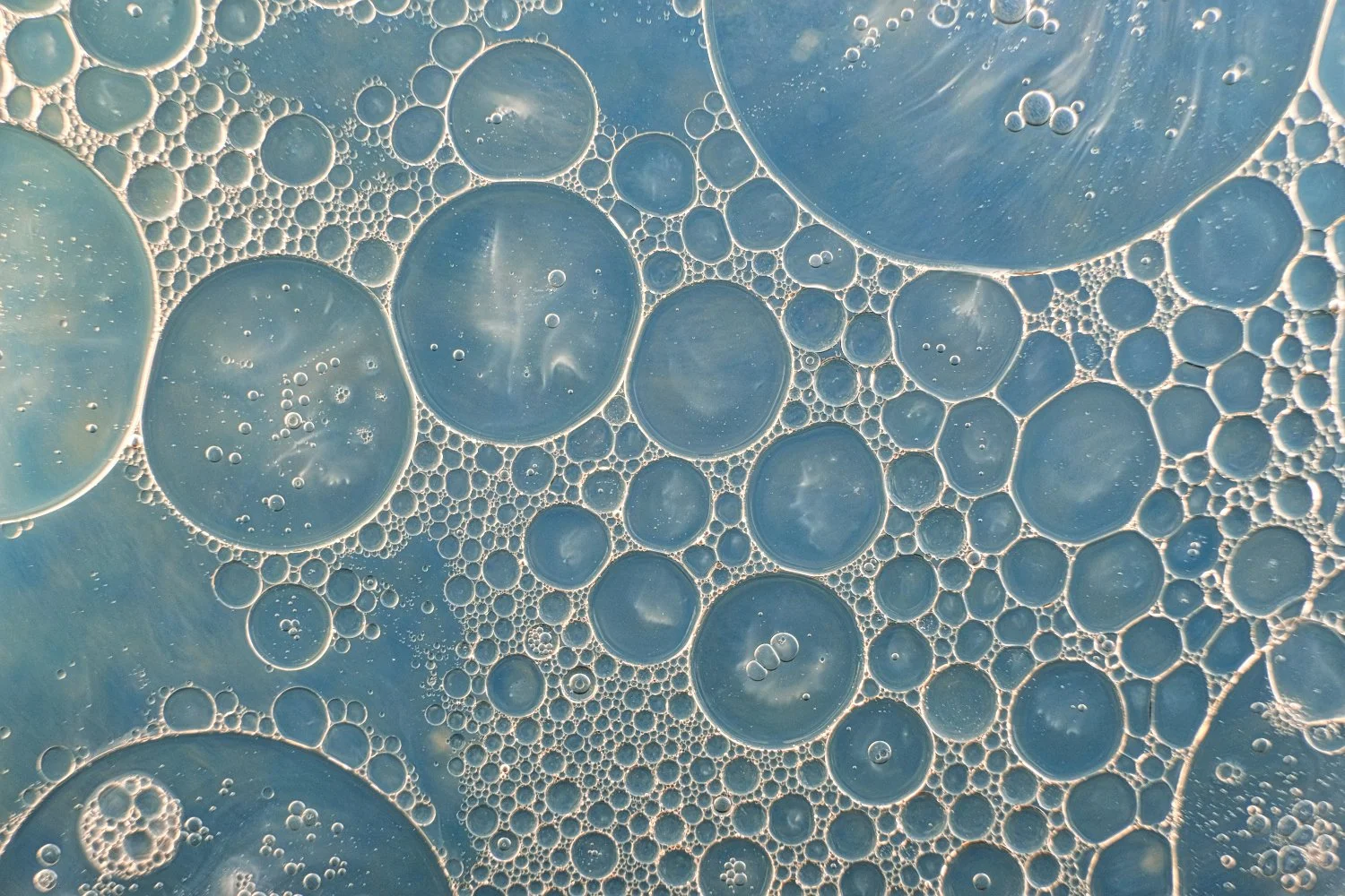 Close-up of oil droplets floating in water, forming various-sized bubbles with a blue background.
