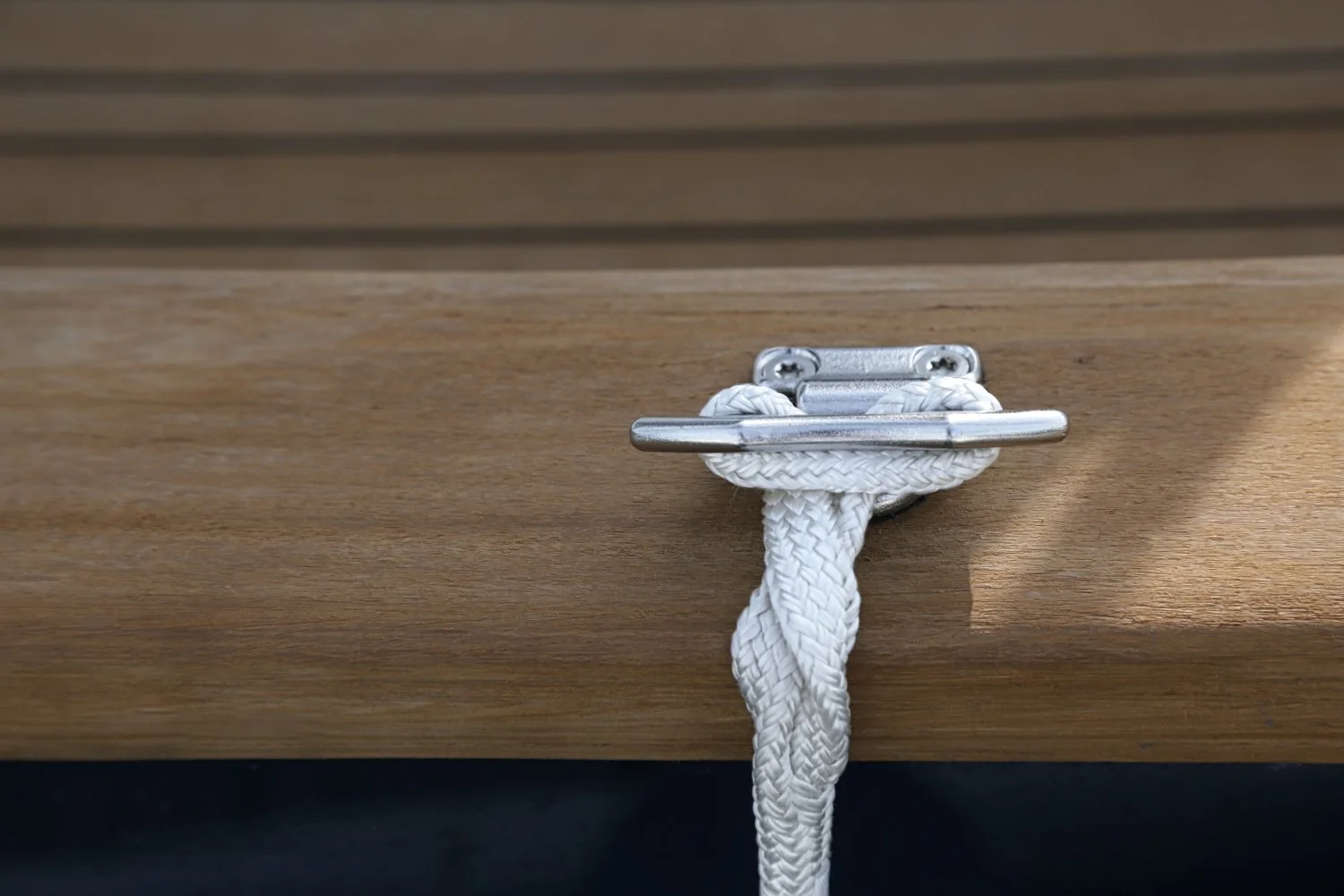Close-up of a metal latch with a white braided rope tied around it, mounted on a wooden surface.