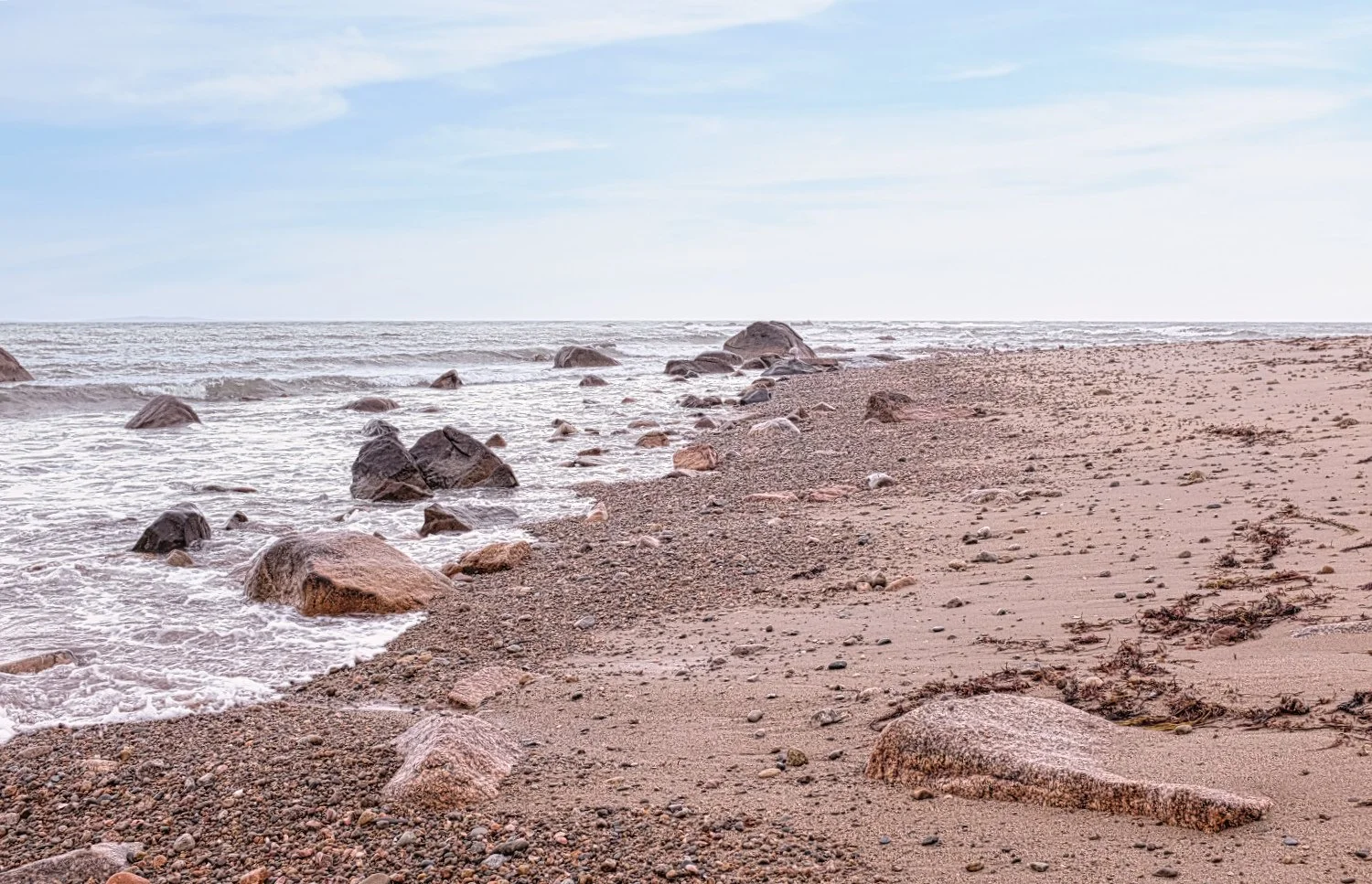 A sandy beach with rocks along the shoreline, gentle waves, and a cloudy sky.