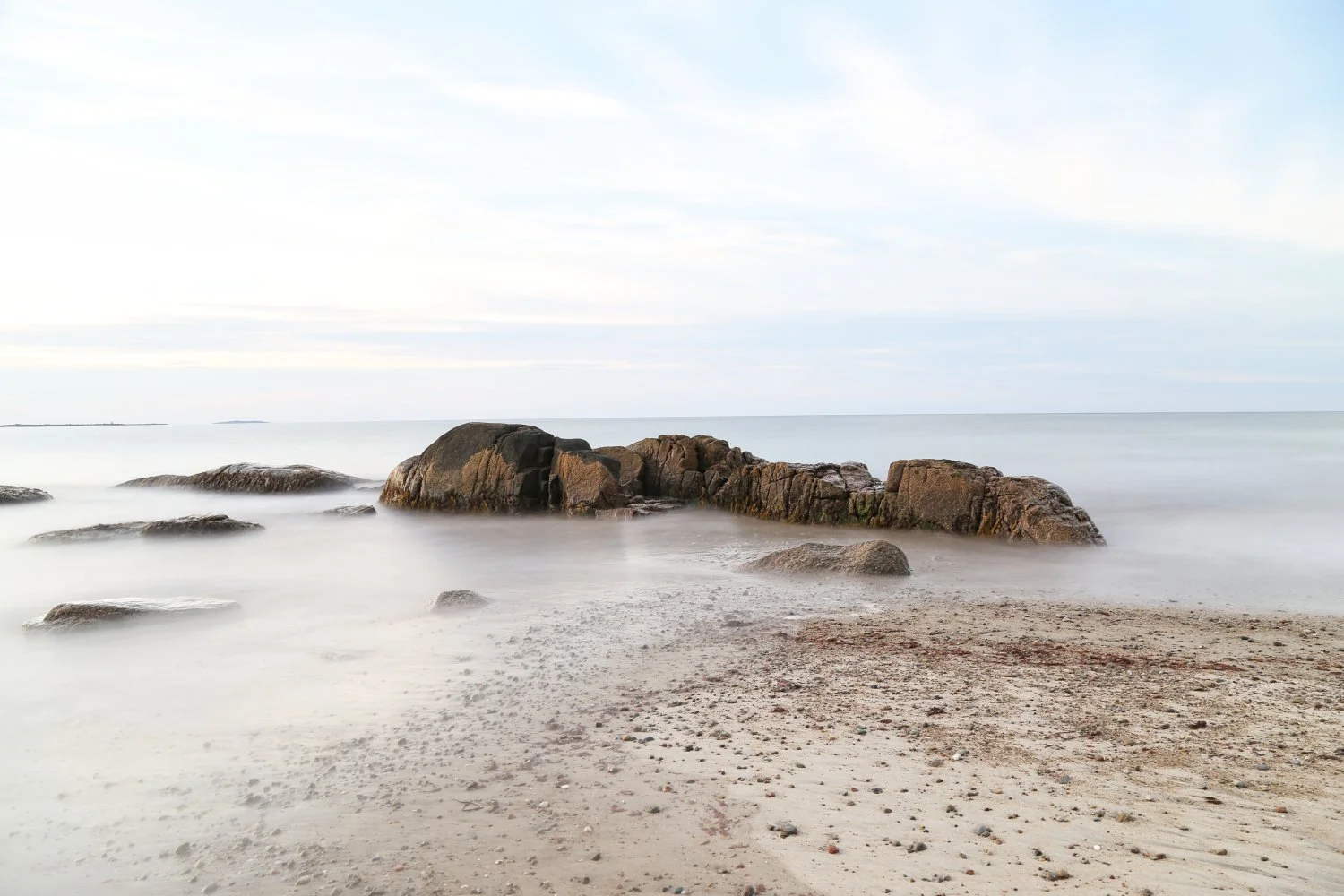 A calm beach scene with rocks in the water and a cloudy sky.