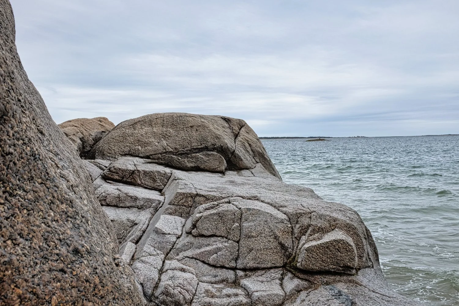 Large rocks along the shoreline with the ocean and cloudy sky in the background.