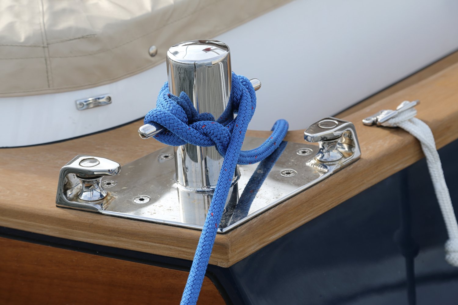 A close-up of a metal cleat on a wooden surface with a blue rope wrapped around it, and a white rope attached nearby, on a boat.