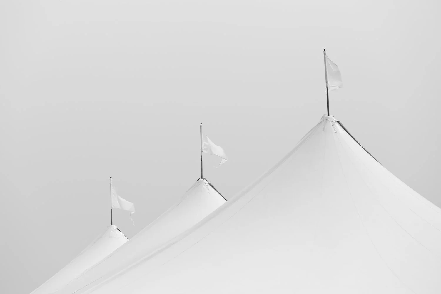 Close-up of the peaked white fabric tents with small flags on top of each peak against a plain sky background.