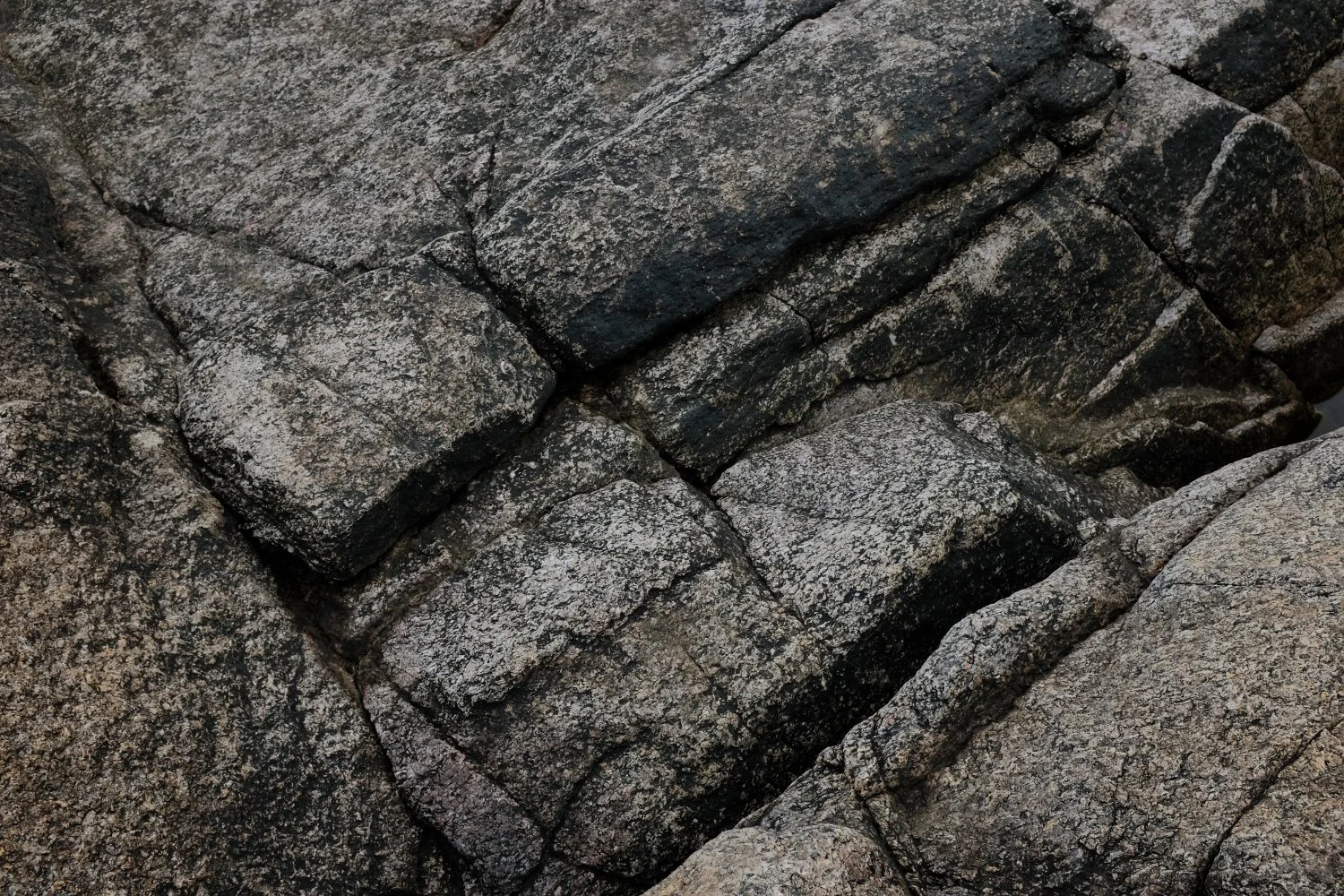 Close-up of dark gray and black textured rocks with cracks and uneven surfaces.