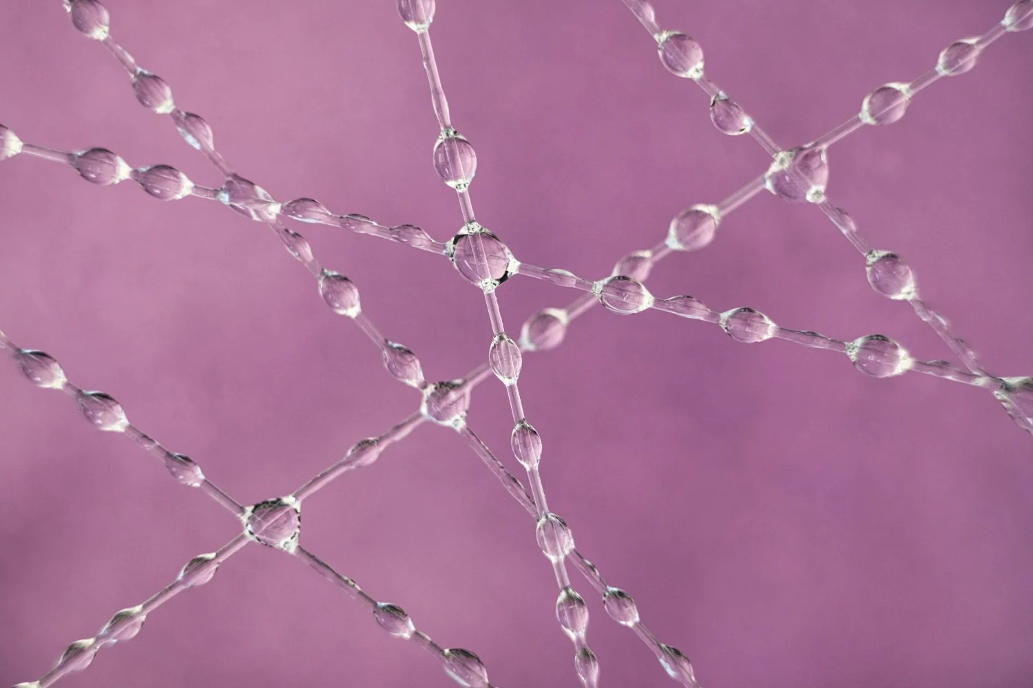 Close-up of delicate, thin chain links with water droplets on a purple background.