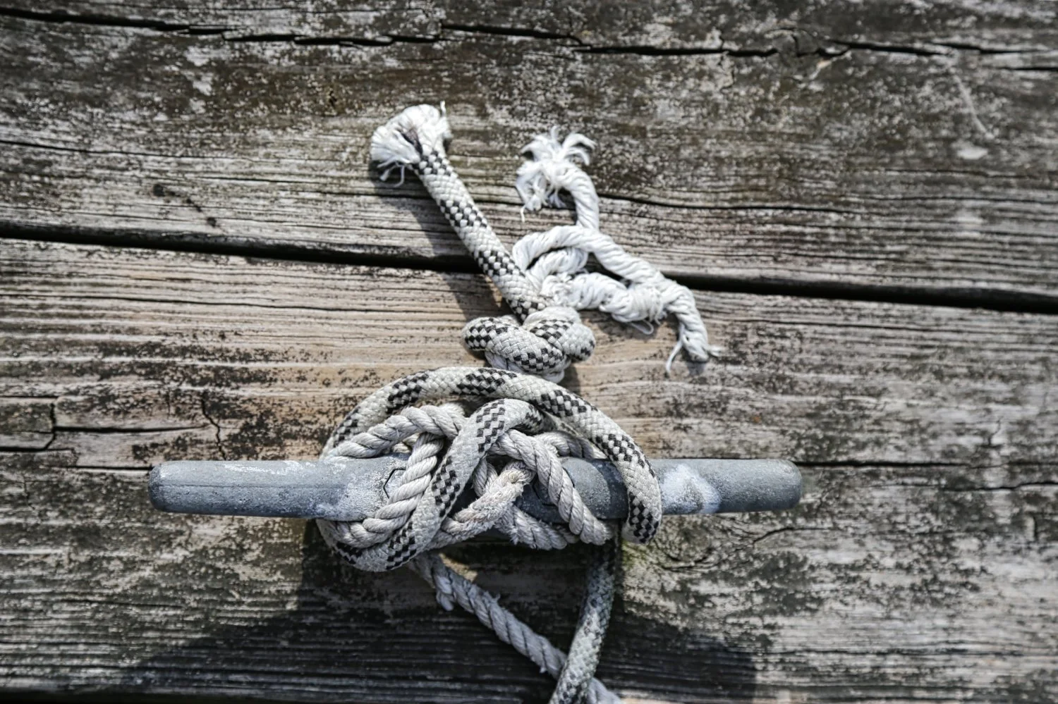 Close-up of a metal hook with tangled white and black patterned ropes on a weathered wooden surface.
