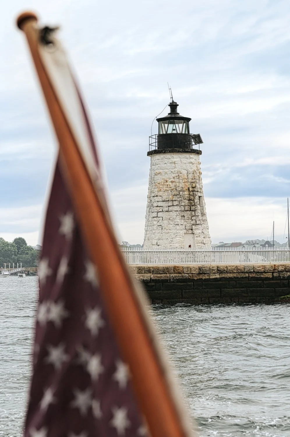View of a lighthouse on the water with an American flag in the foreground.