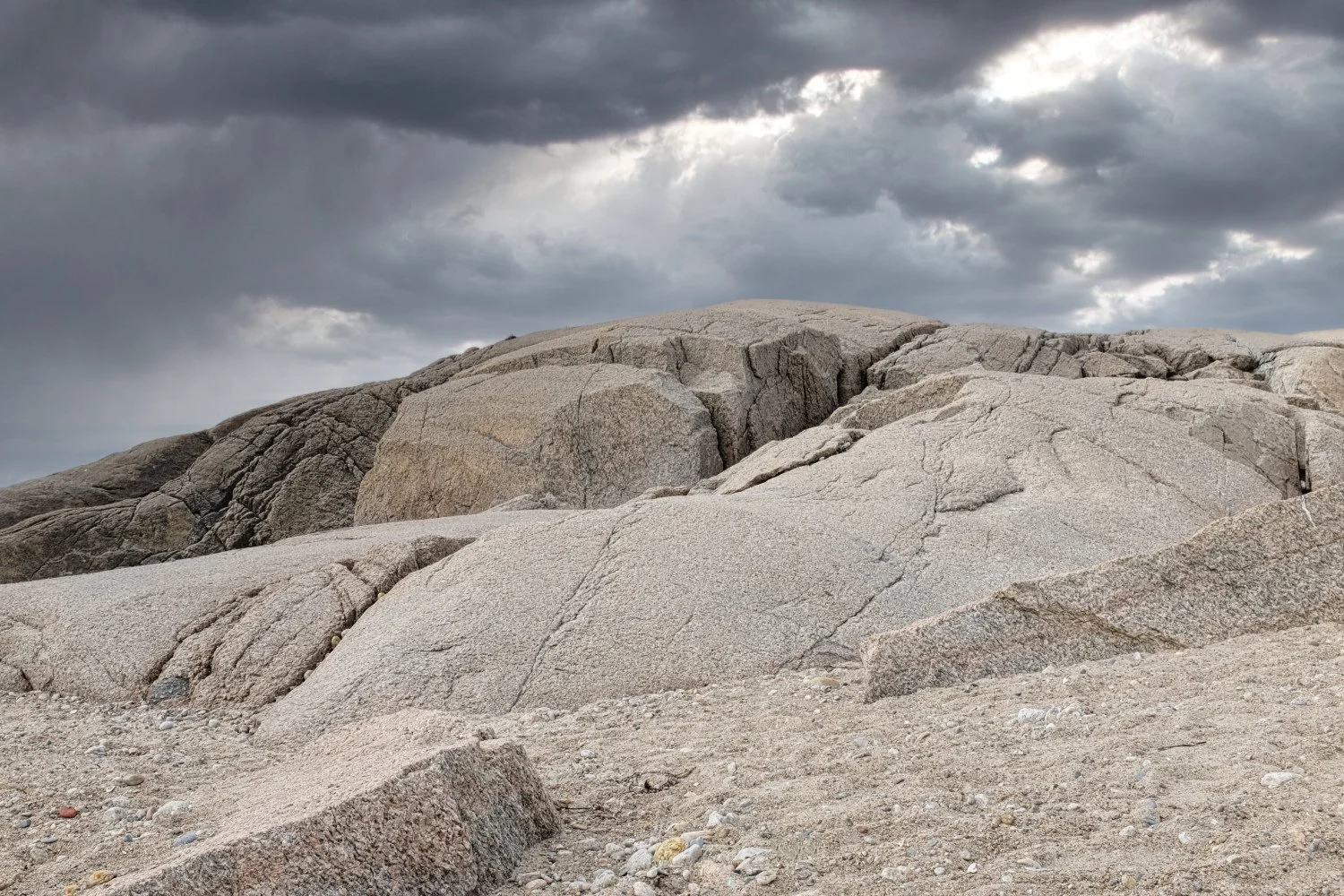 Large, weathered granite rocks and boulders on a sandy, gravelly terrain under a cloudy, dark sky.
