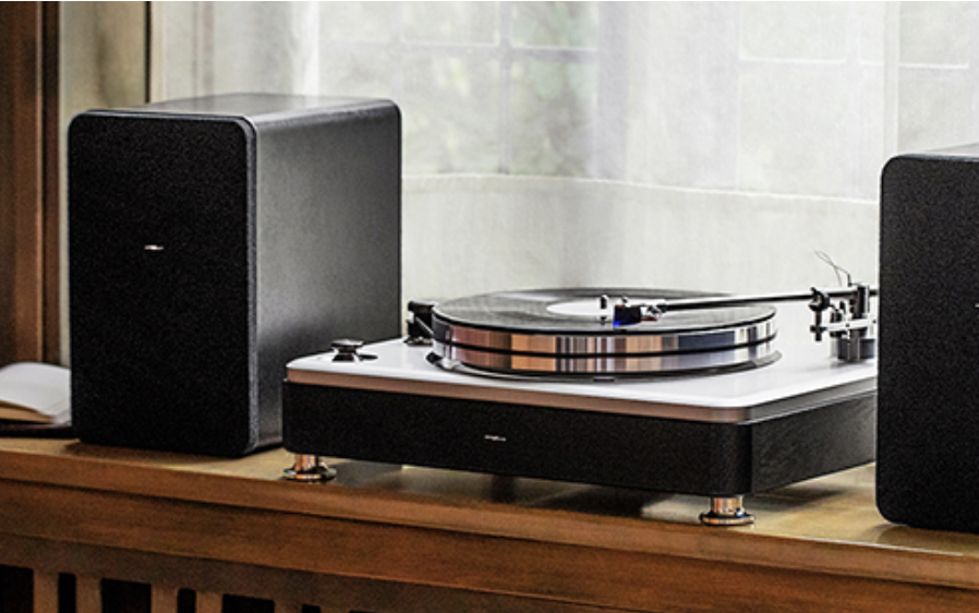 A record player with two black speakers on a wooden surface near a window.