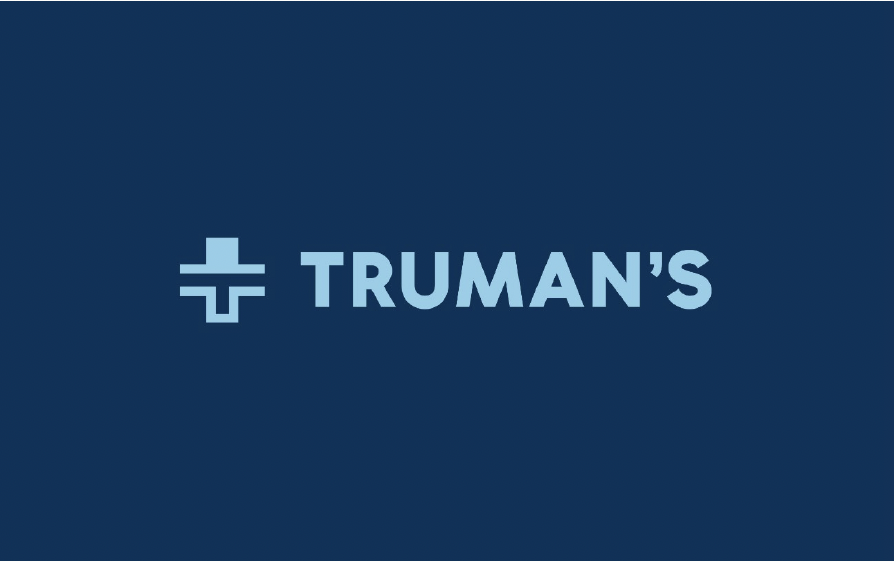 A dark blue background with the word 'TRUMAN'S' in light blue capital letters, accompanied by a logo consisting of a stylized cross with horizontal and vertical bars.