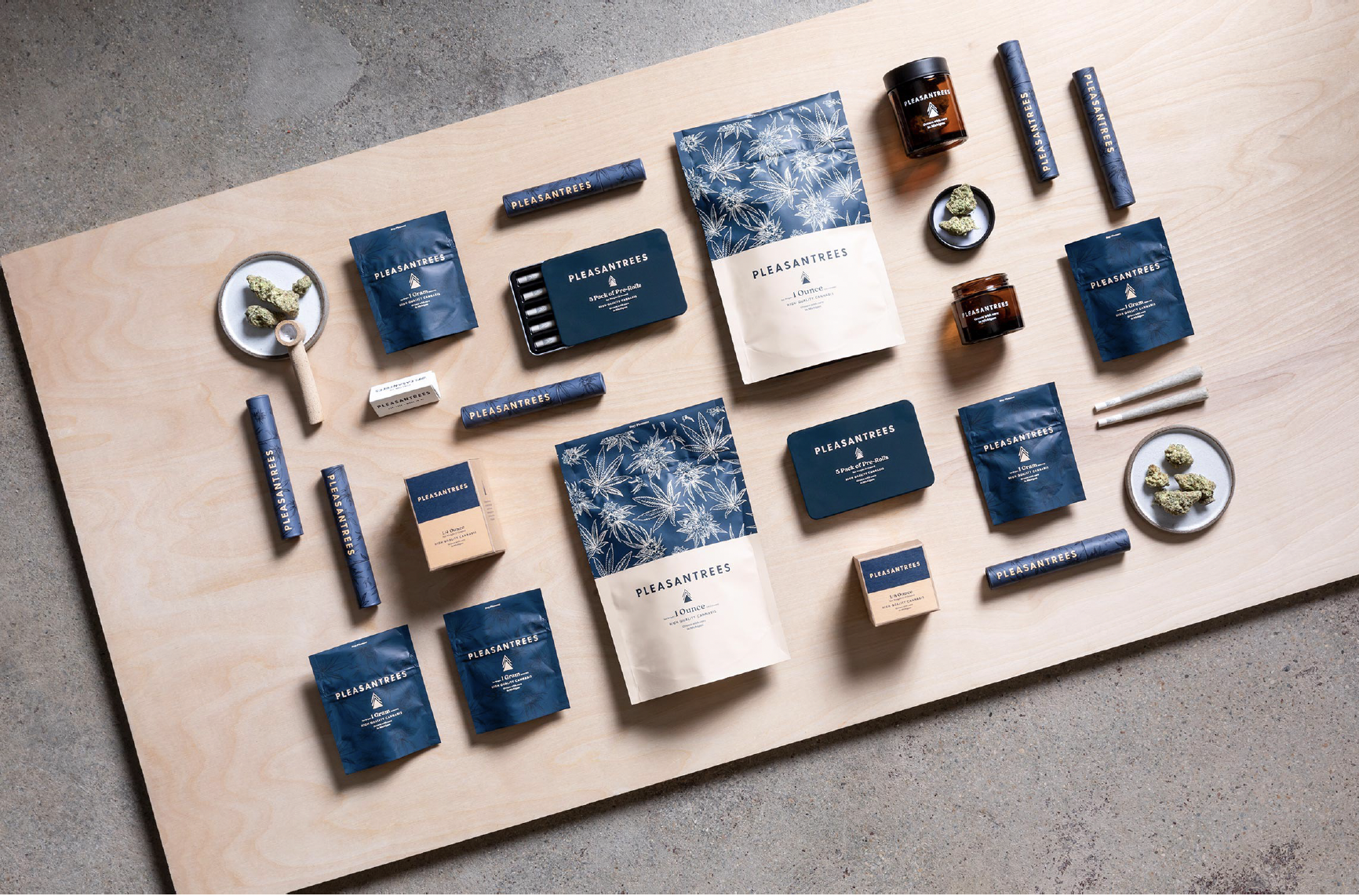 Assorted cannabis products and accessories on a wooden table, including cigar wraps, pre-rolls, jars of cannabis, and small dishes with cannabis buds.