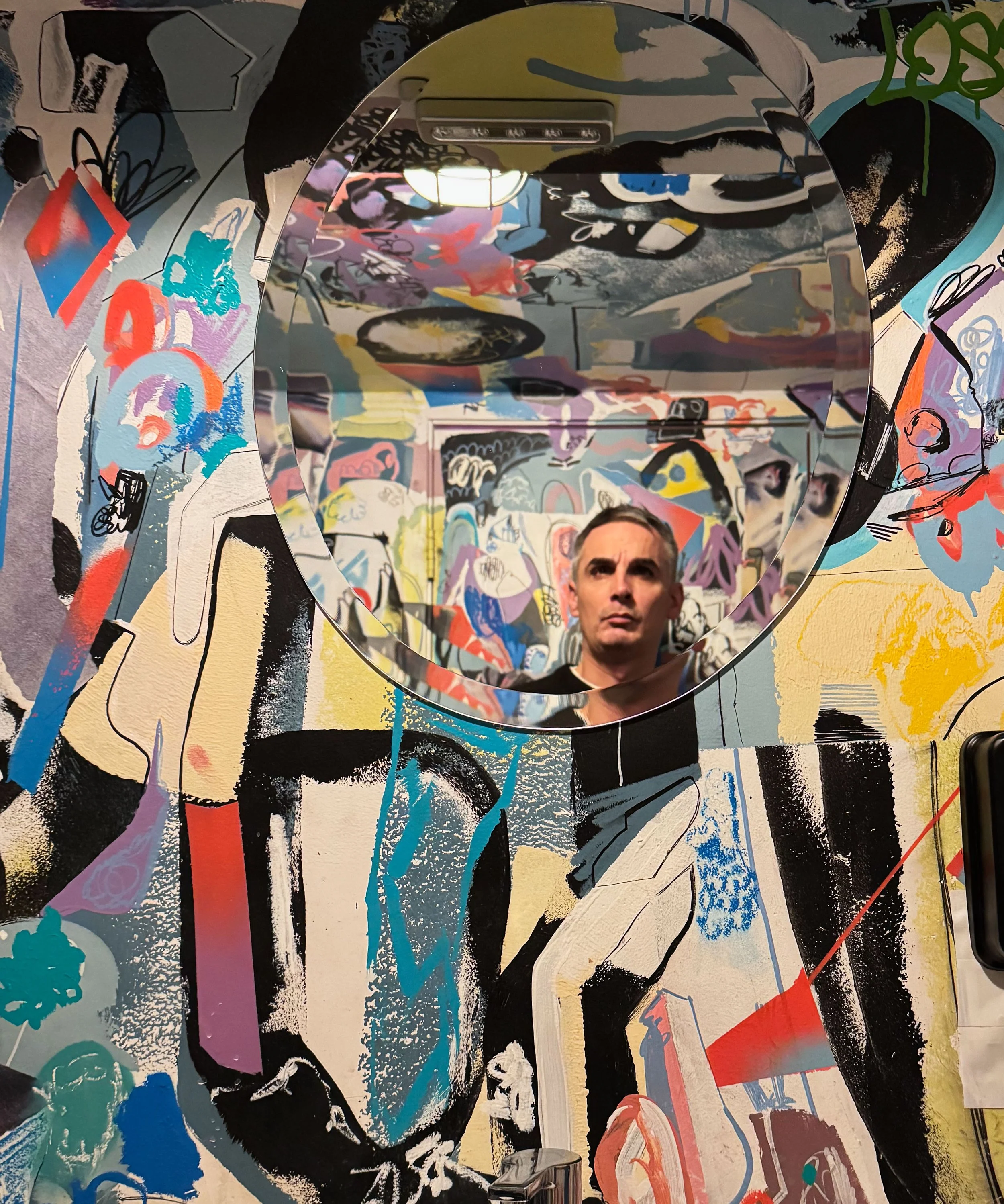 A colorful abstract mural featuring a large eye with black and white detailing, surrounded by vibrant splashes of paint, graffiti, and varied shapes.