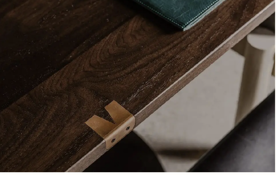 Close-up of a wooden table with a piece of tape and small black screws attached to a metal bracket.